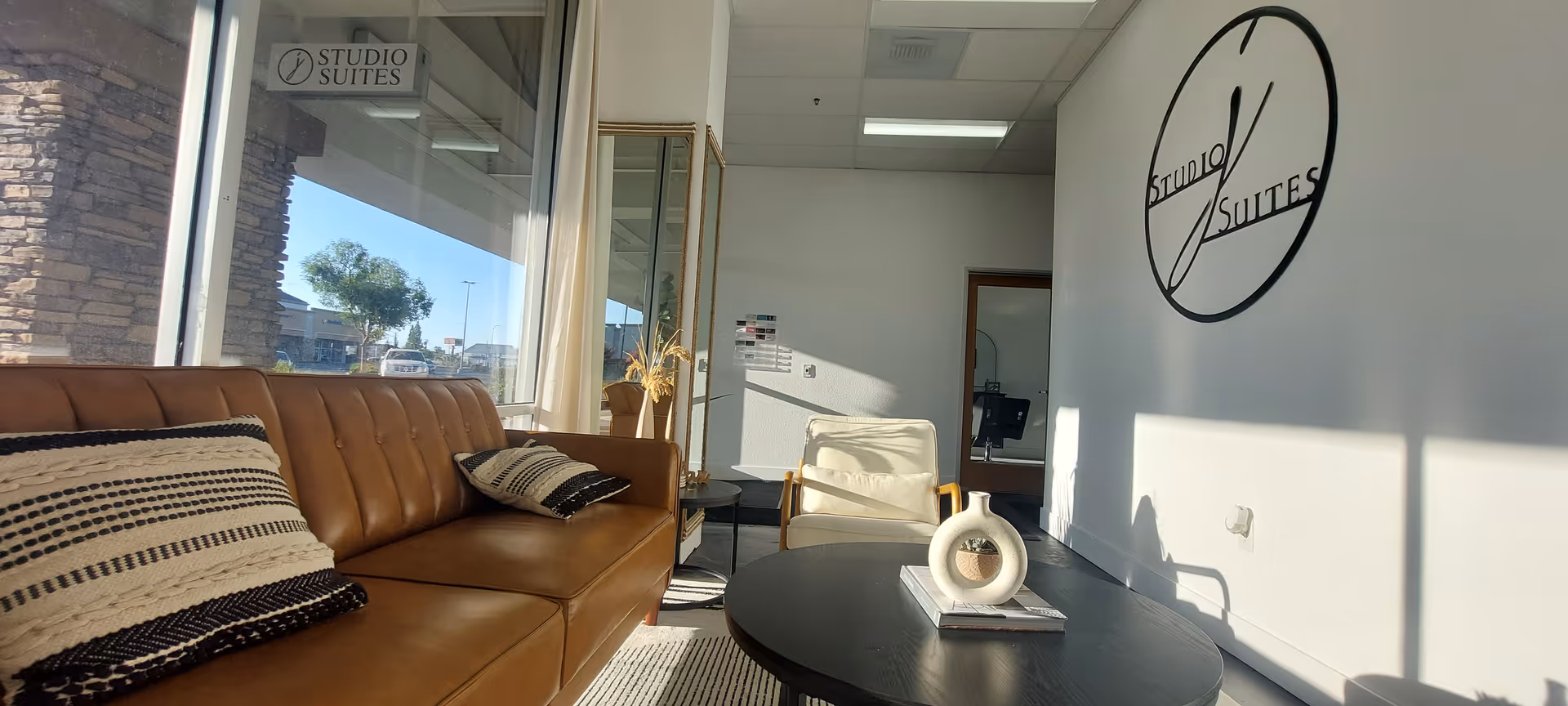 Bright lounge area with tan leather sofa, round coffee table, and Studio Suites logo wall.