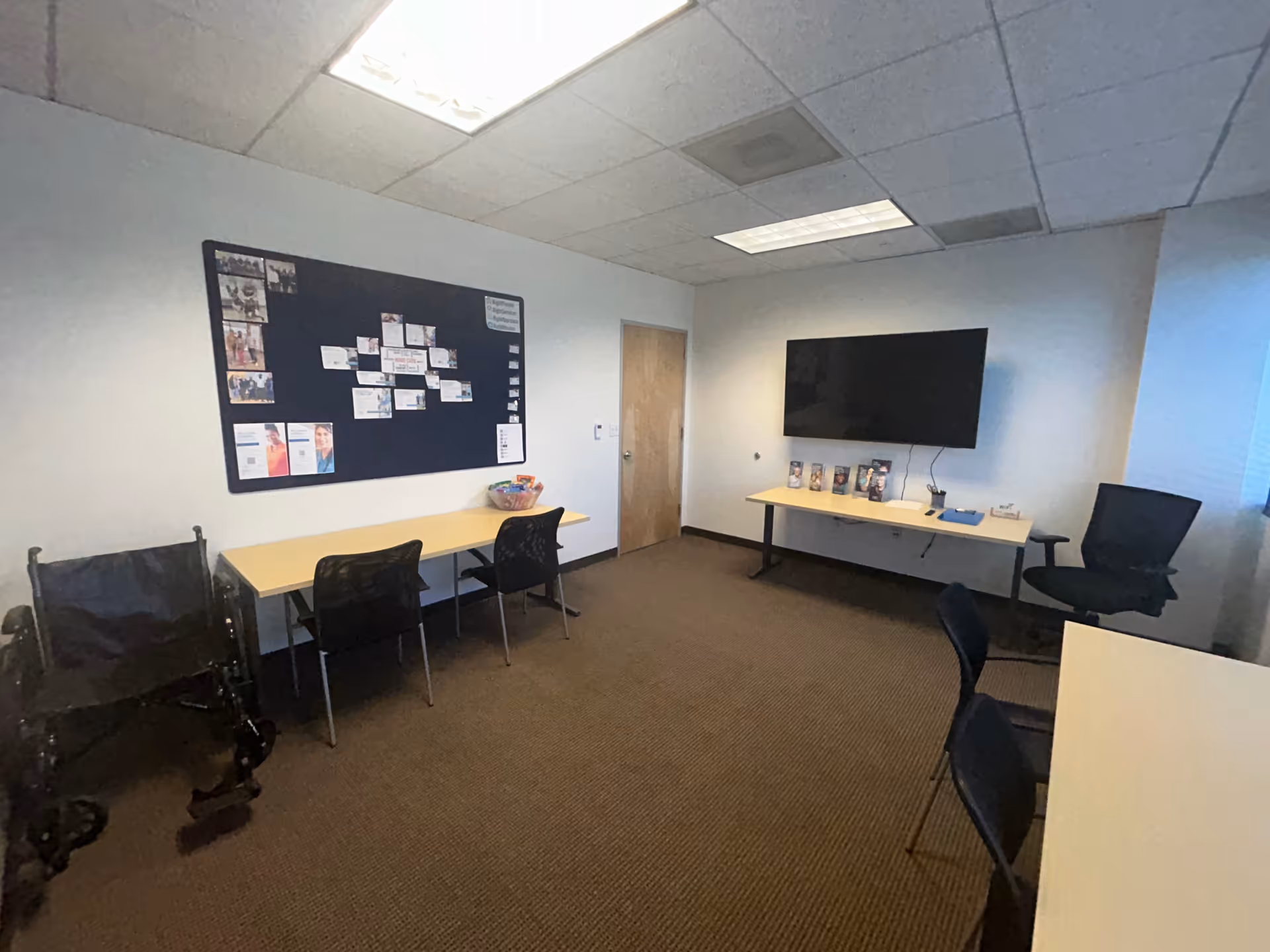 Interior conference room with long desk and chairs, bulletin board, and wall-mounted TV.