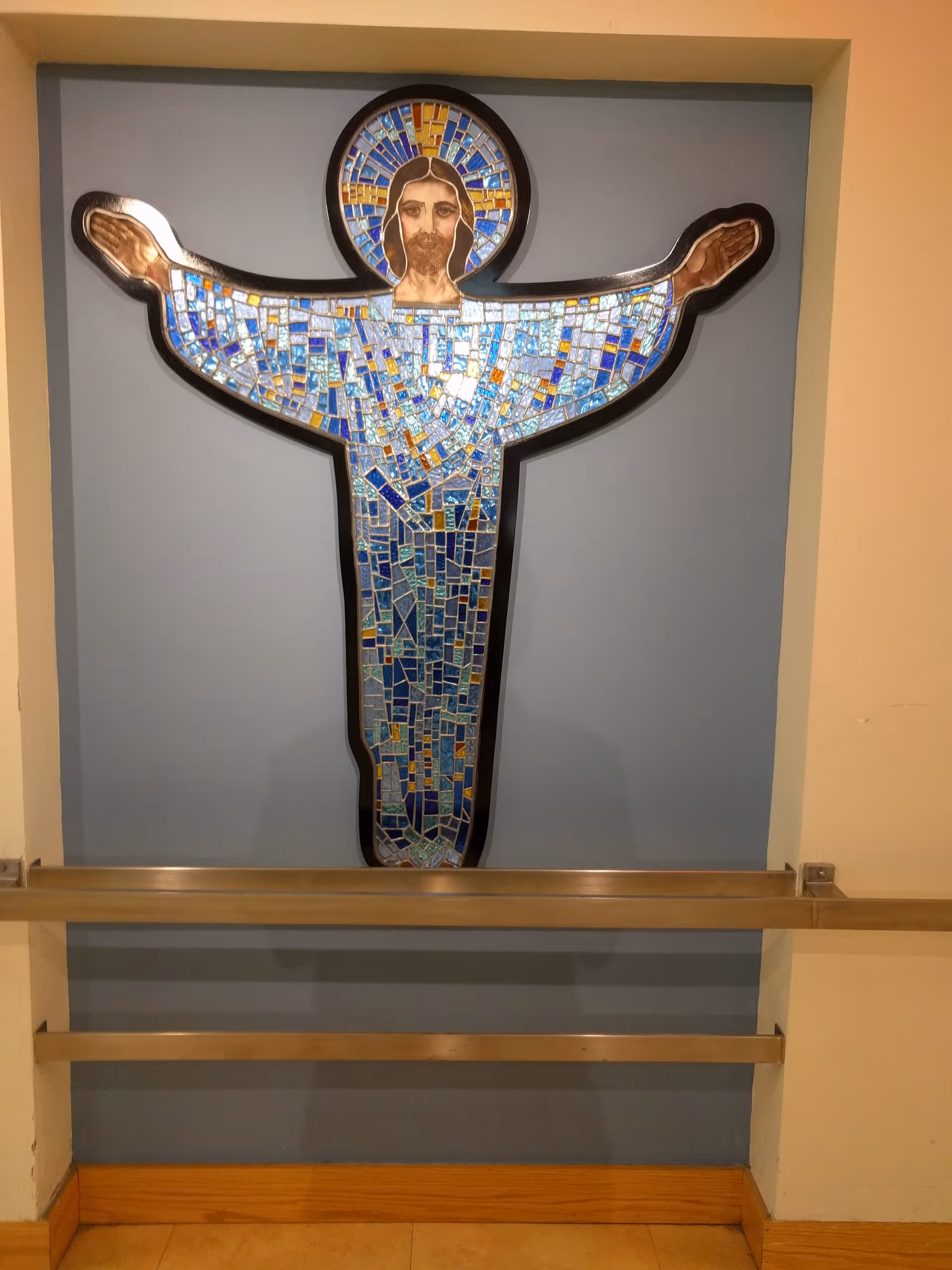 Mosaic Jesus wall mural on blue interior hallway, with a wooden railing along the base.