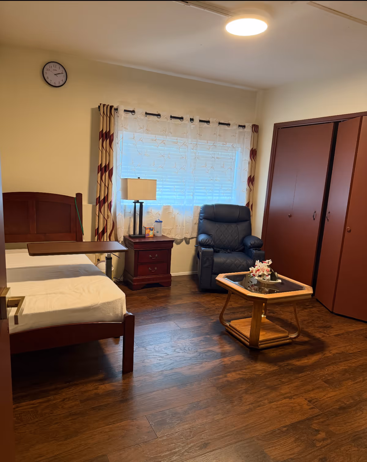A cozy senior living bedroom with a bed, armchair, window, and wardrobe.