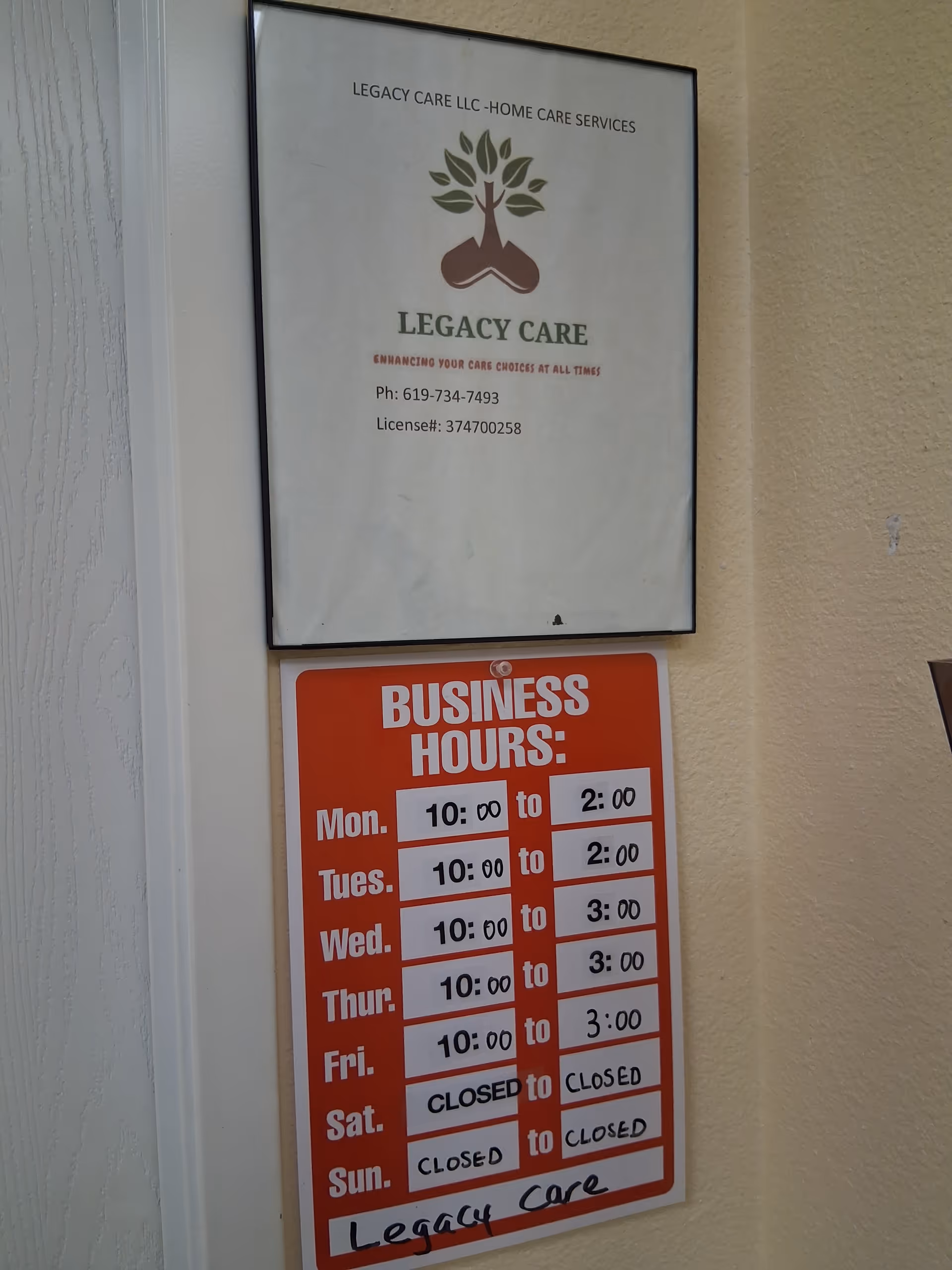 A framed sign and a red business hours board mounted on a beige hallway wall.