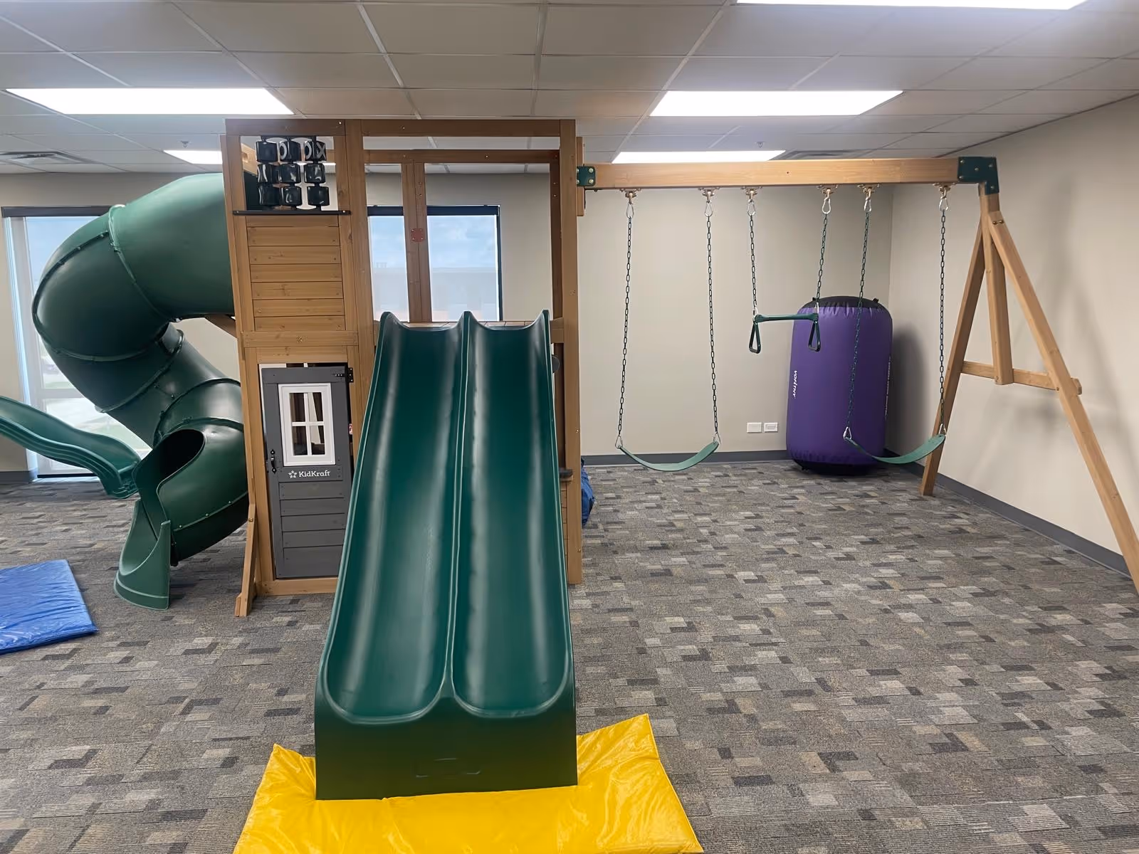 Indoor play area with green slides, swings, and a purple punching bag.