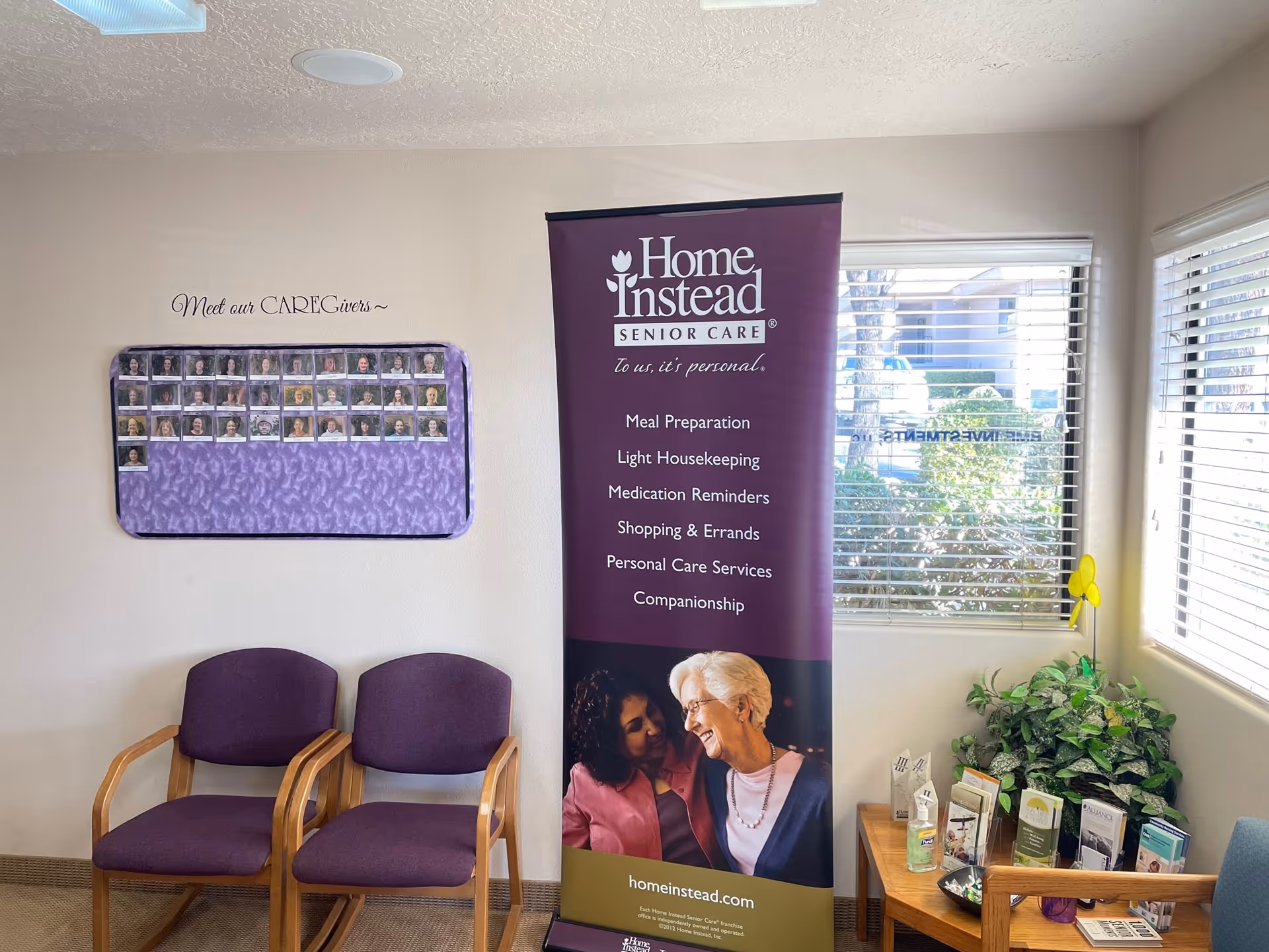 Interior lounge with a purple Home Instead banner, two purple chairs, and brochures.