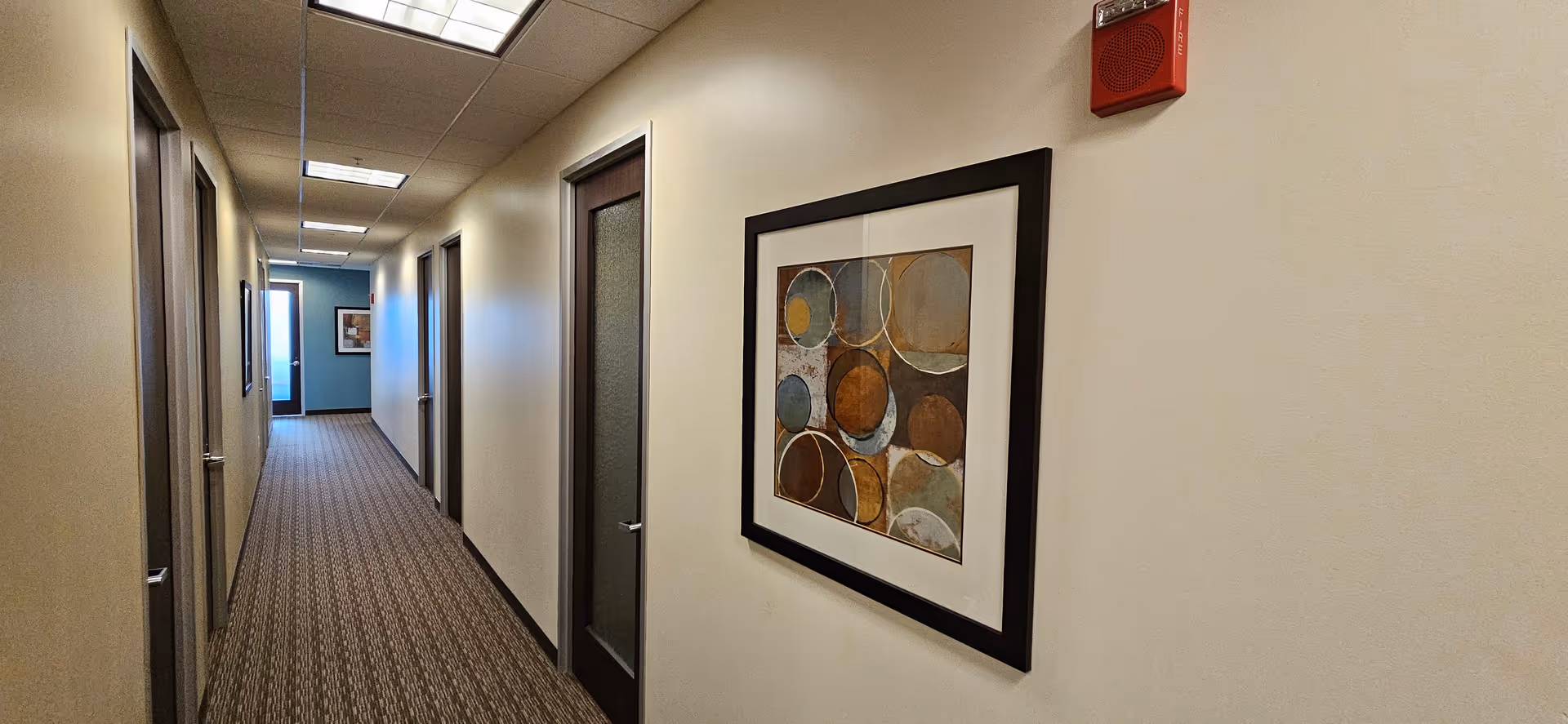 Long hallway in a senior living facility with doors and framed wall art.