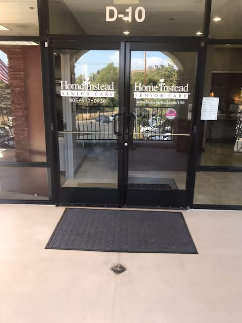 Glass entrance doors labeled Home Instead Senior Care, with D-10 above and a front walkway mat.