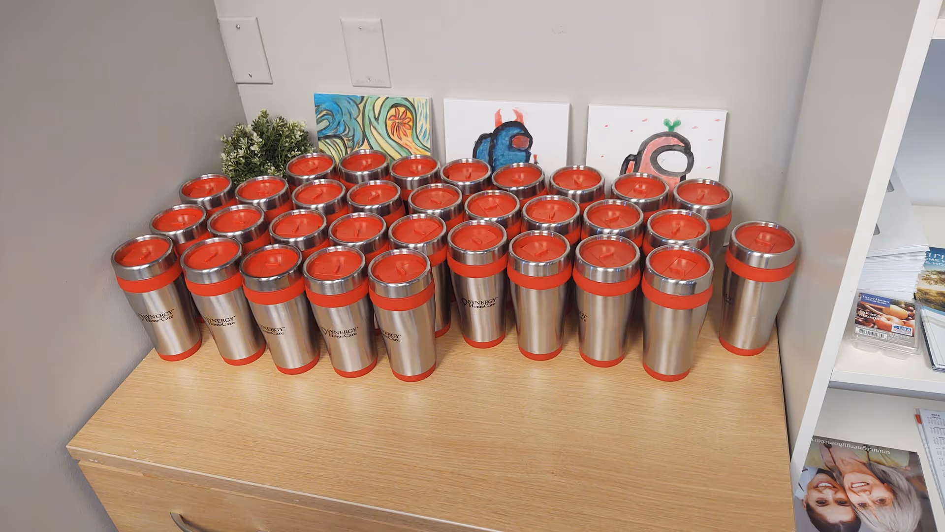 Row of stainless steel tumblers with red lids arranged on a wooden cabinet.
