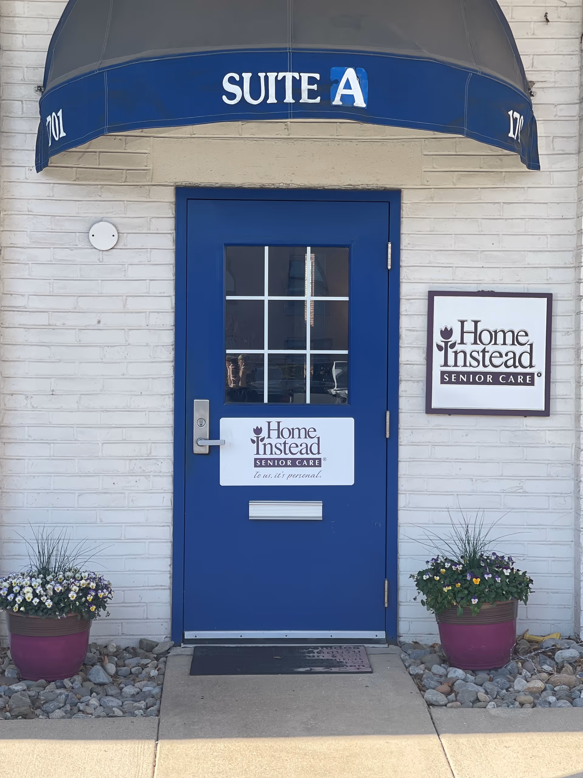 Blue door with glass panes under Suite A awning, Home Instead sign, and potted flowers.