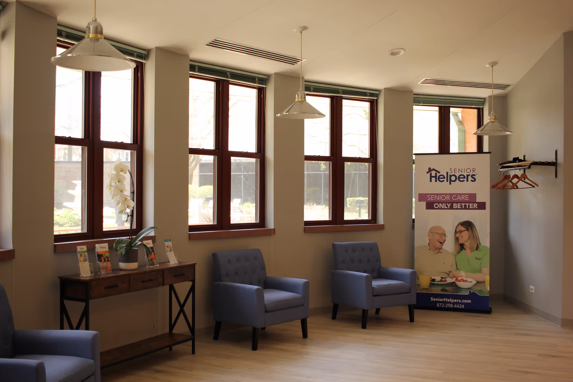 Interior lounge area with blue chairs, a wooden console, large windows, and a Senior Helpers banner.