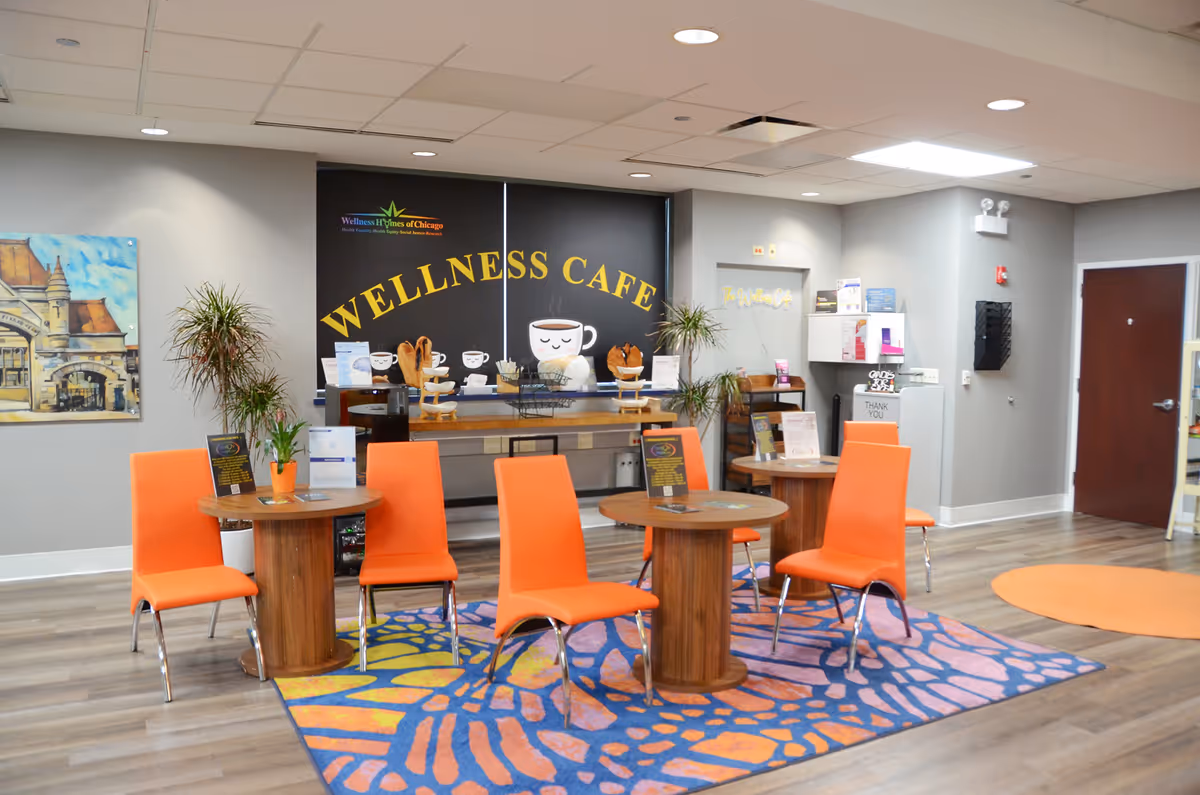 Bright wellness cafe seating area with orange chairs around round tables and a colorful rug.