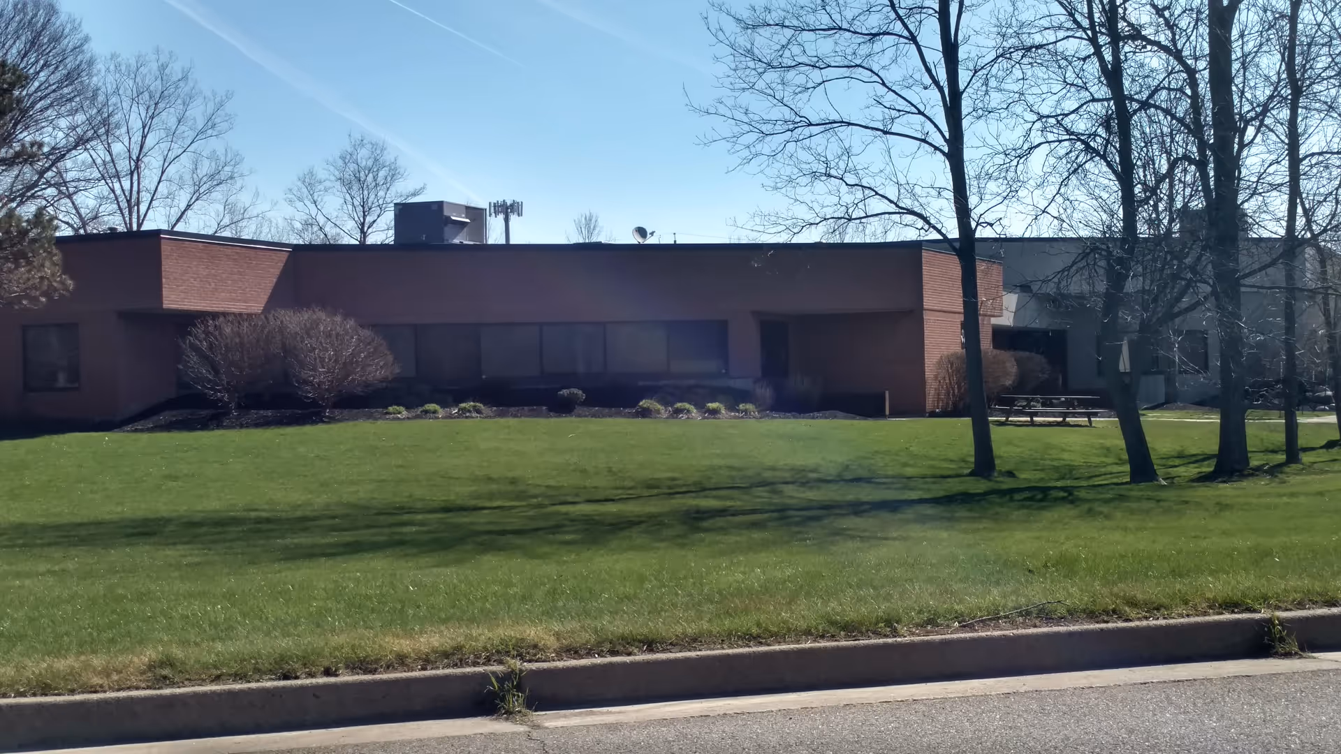 Exterior view of a single-story brick senior living facility with a grassy lawn and trees.