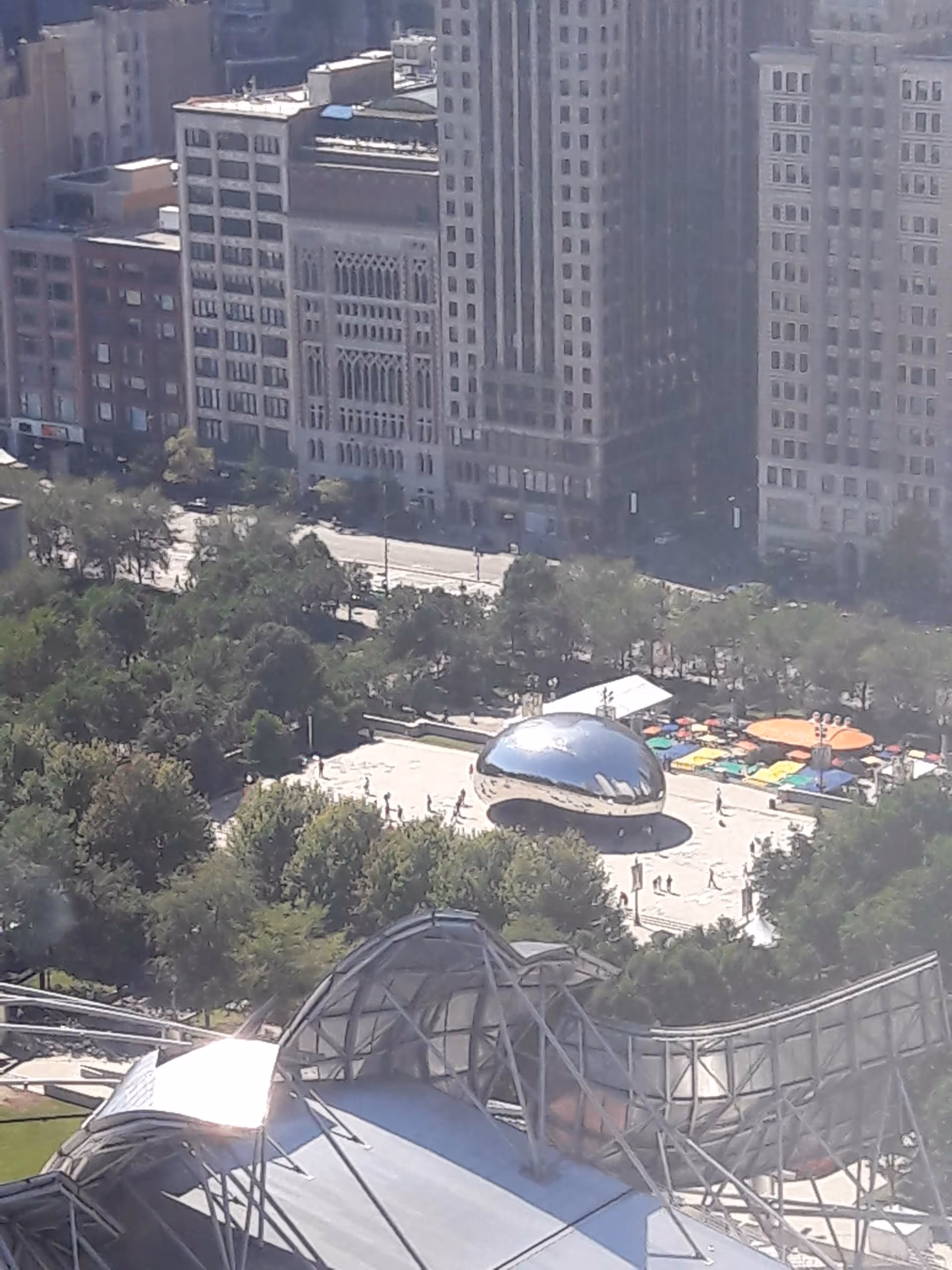 Cityscape with tall buildings, trees, and a reflective dome sculpture in a busy plaza.