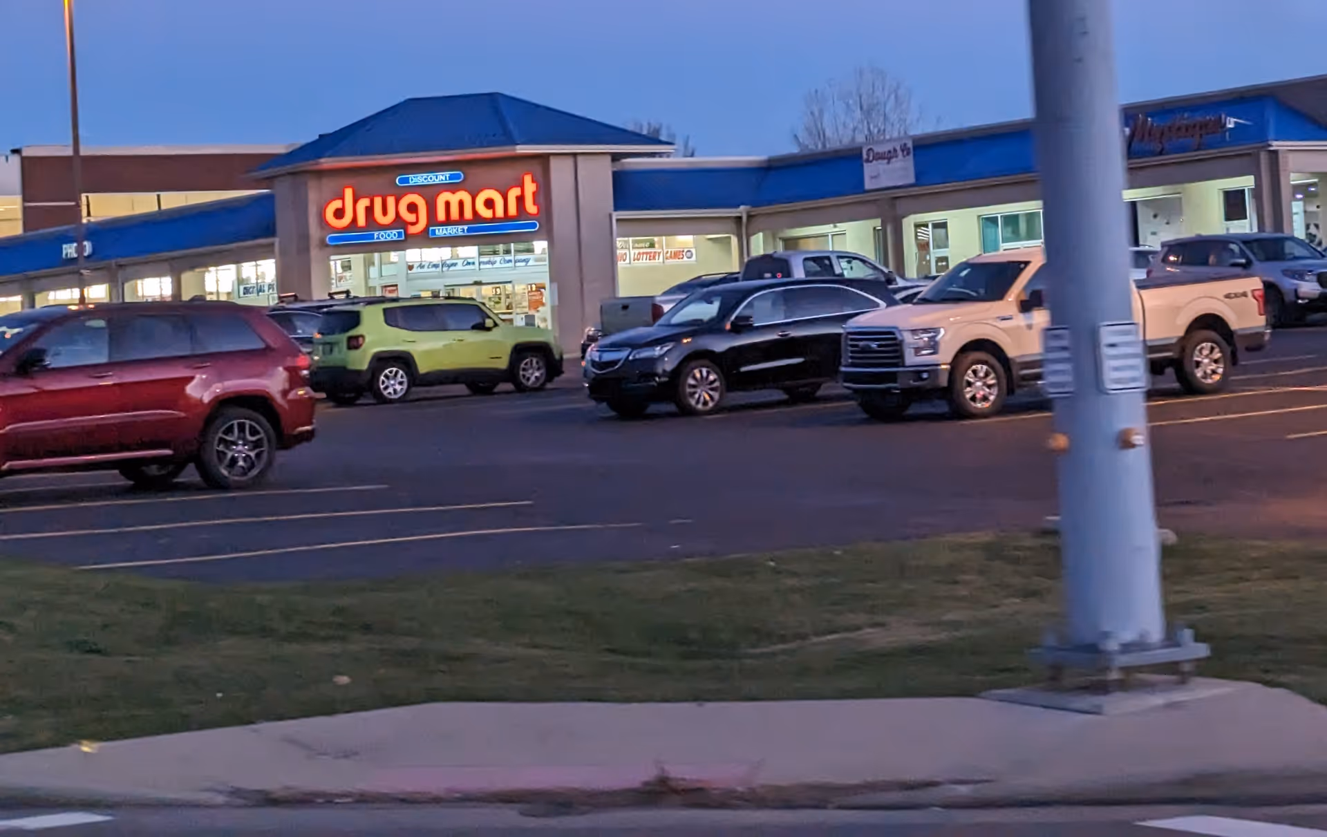 Discount Drug Mart storefront in a strip mall parking lot with multiple parked cars.