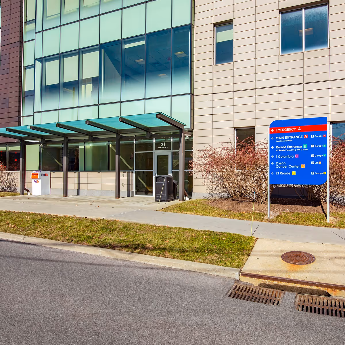 Modern glass-front medical center entrance with blue sign and shaded walkway.