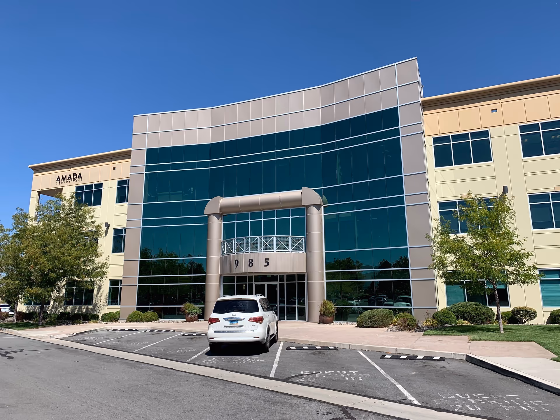 Amada Senior Care building exterior with glass facade and a parked white SUV at entrance.