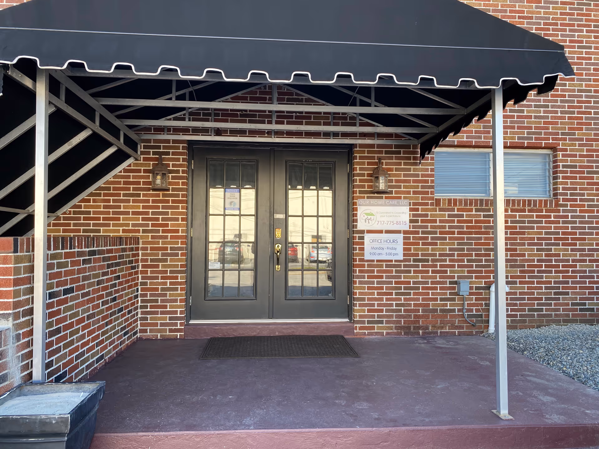 Brick building entrance with double black doors under a black awning and brick exterior.