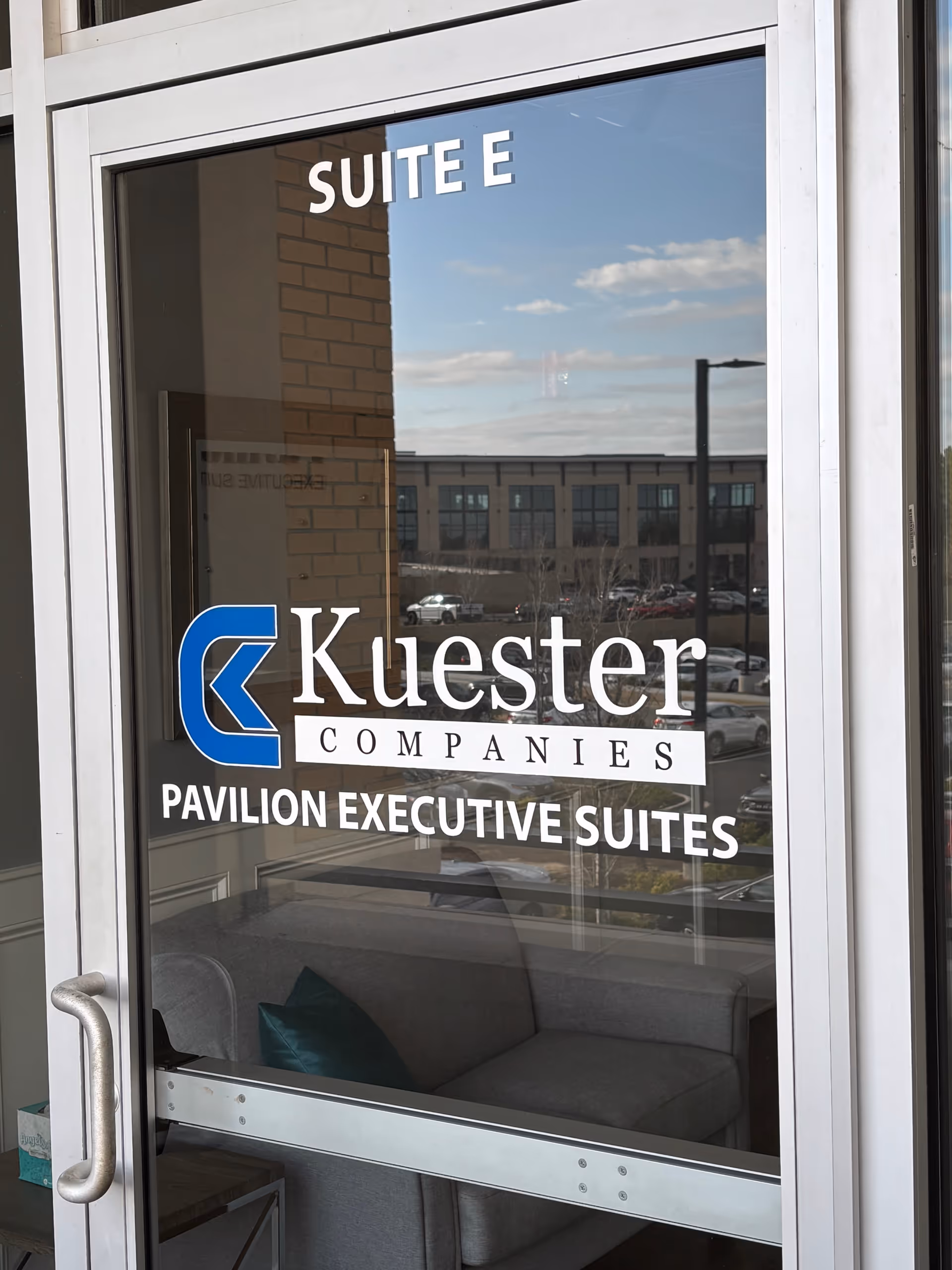 Glass door entry showing Suite E and Kuester Companies signage with a seating area inside.