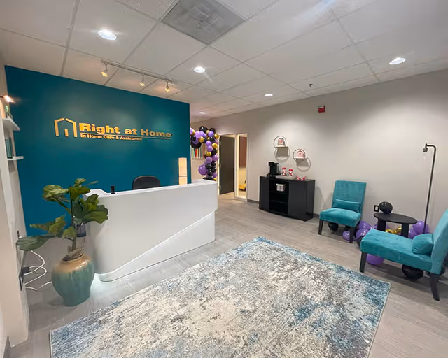 Reception area with teal wall, white desk, and teal chairs in Right at Home lobby.
