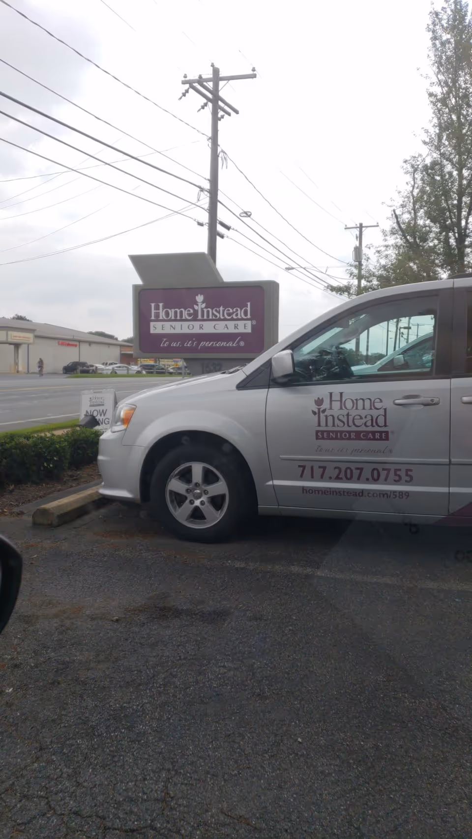 A Home Instead Senior Care van parked beside an outdoor facility sign.