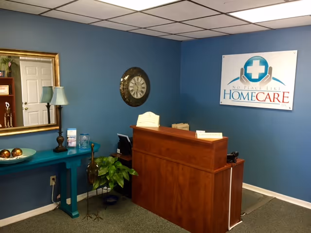 Reception area with wooden desk, blue walls, clock, mirror, and No Place Like Home Care sign.