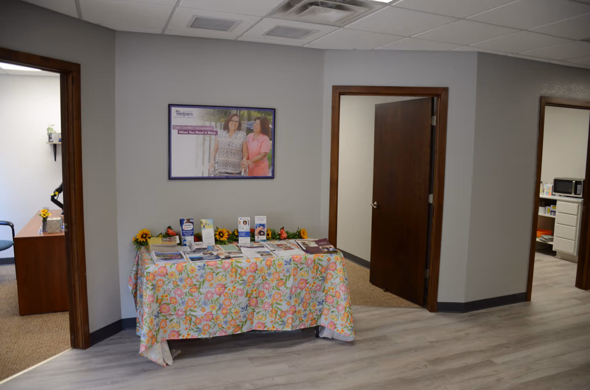 Interior hallway with a floral brochure table and open office doors at Senior Helpers.