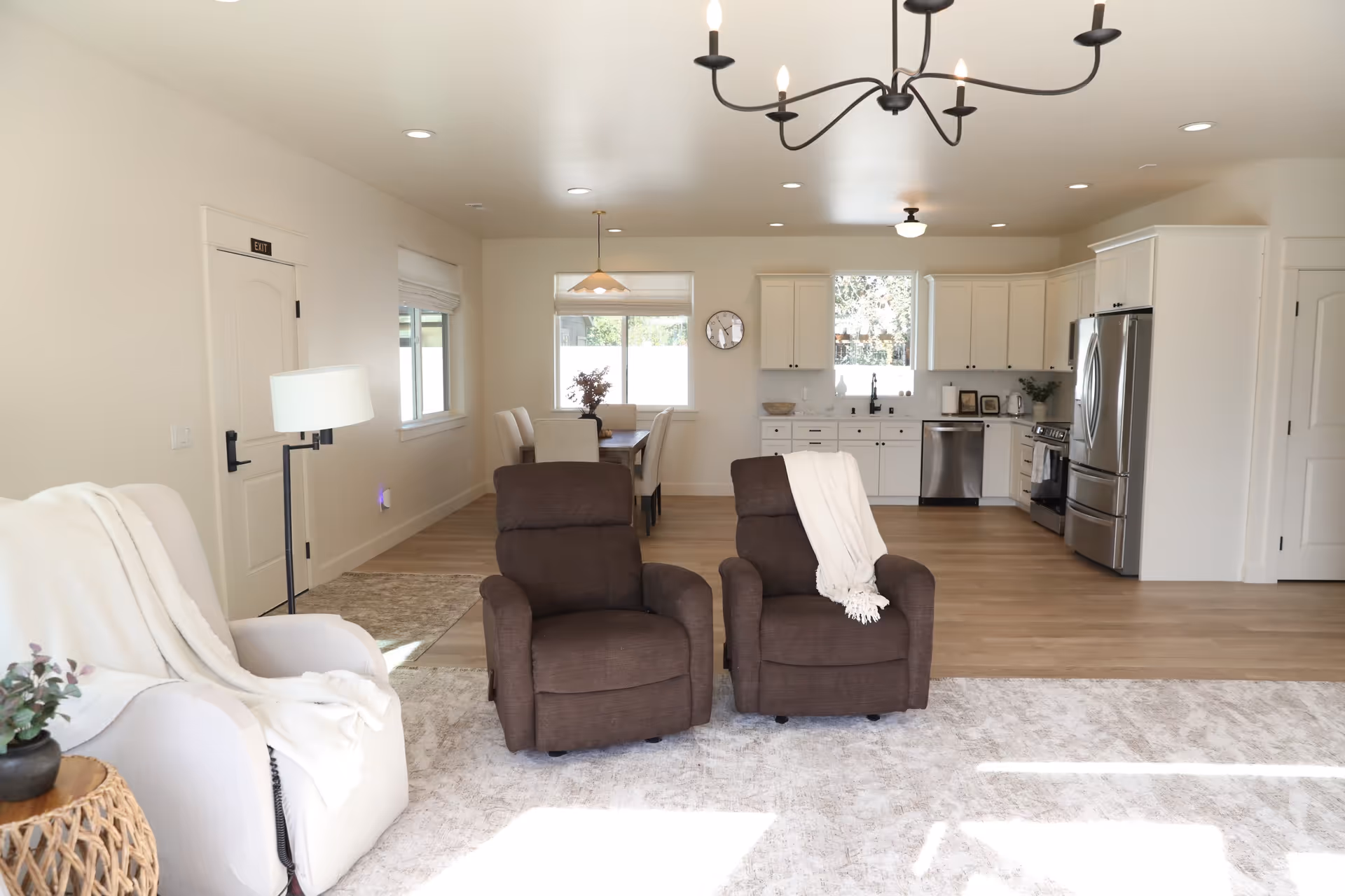 Bright open living area with two recliners, a white sofa, and a kitchen in back.