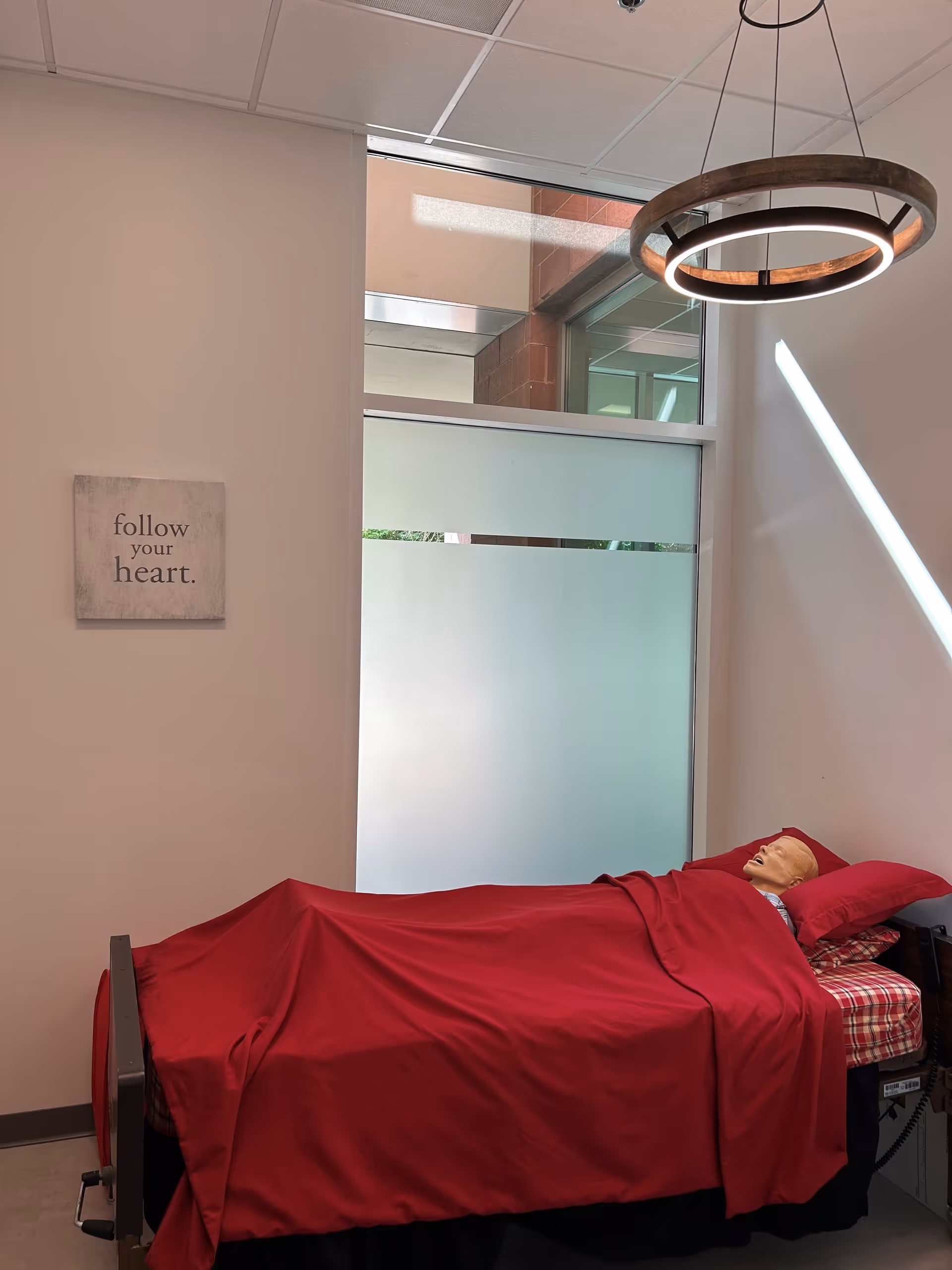 Hospital-style bed with red sheets in a clean interior room of a senior care facility.