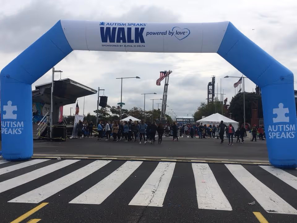 Blue inflatable arch reads Autism Speaks, arches over a crosswalk with a crowd at outdoor walk.