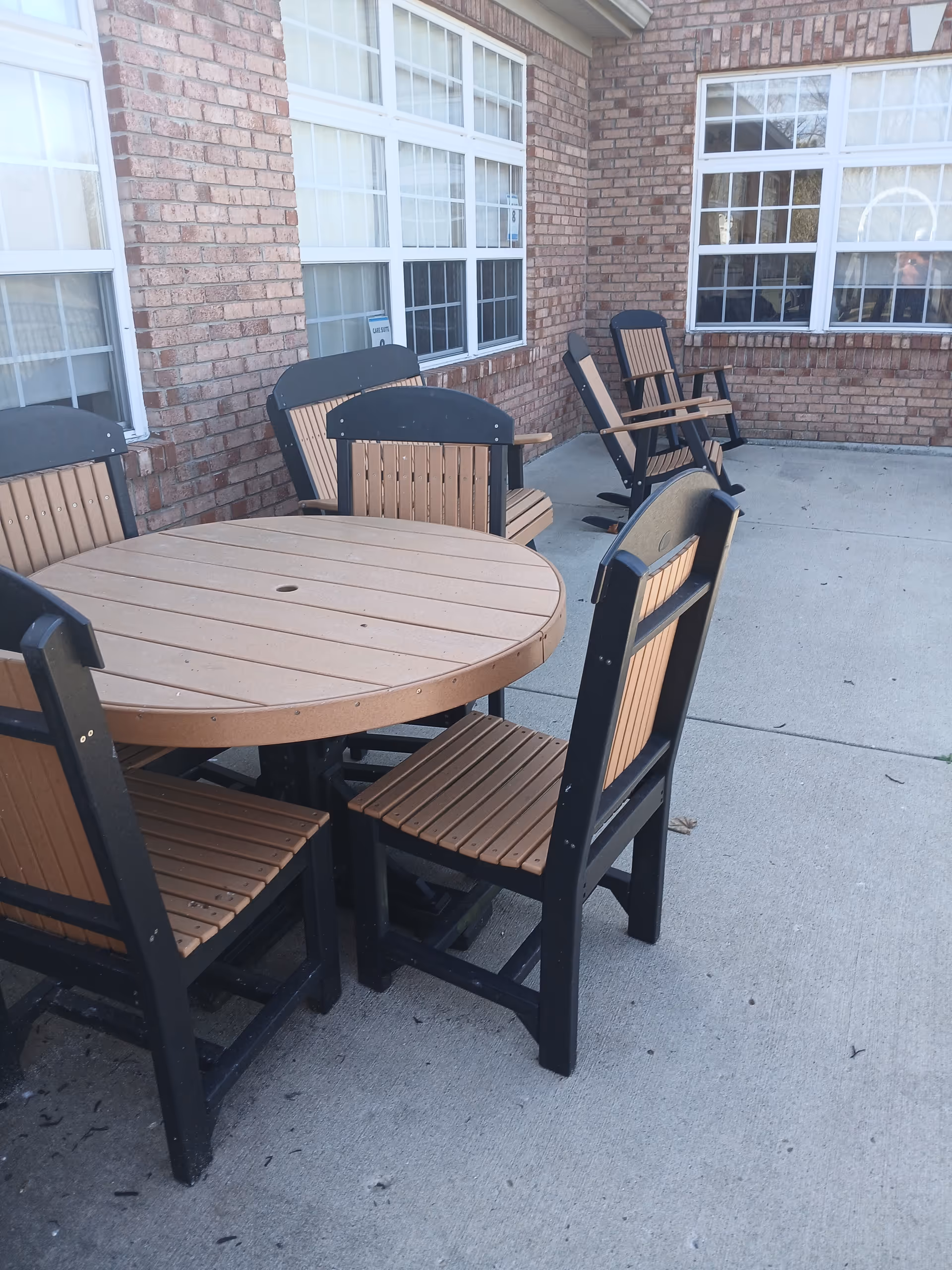 Outdoor patio with round wooden table and chairs beside brick building.
