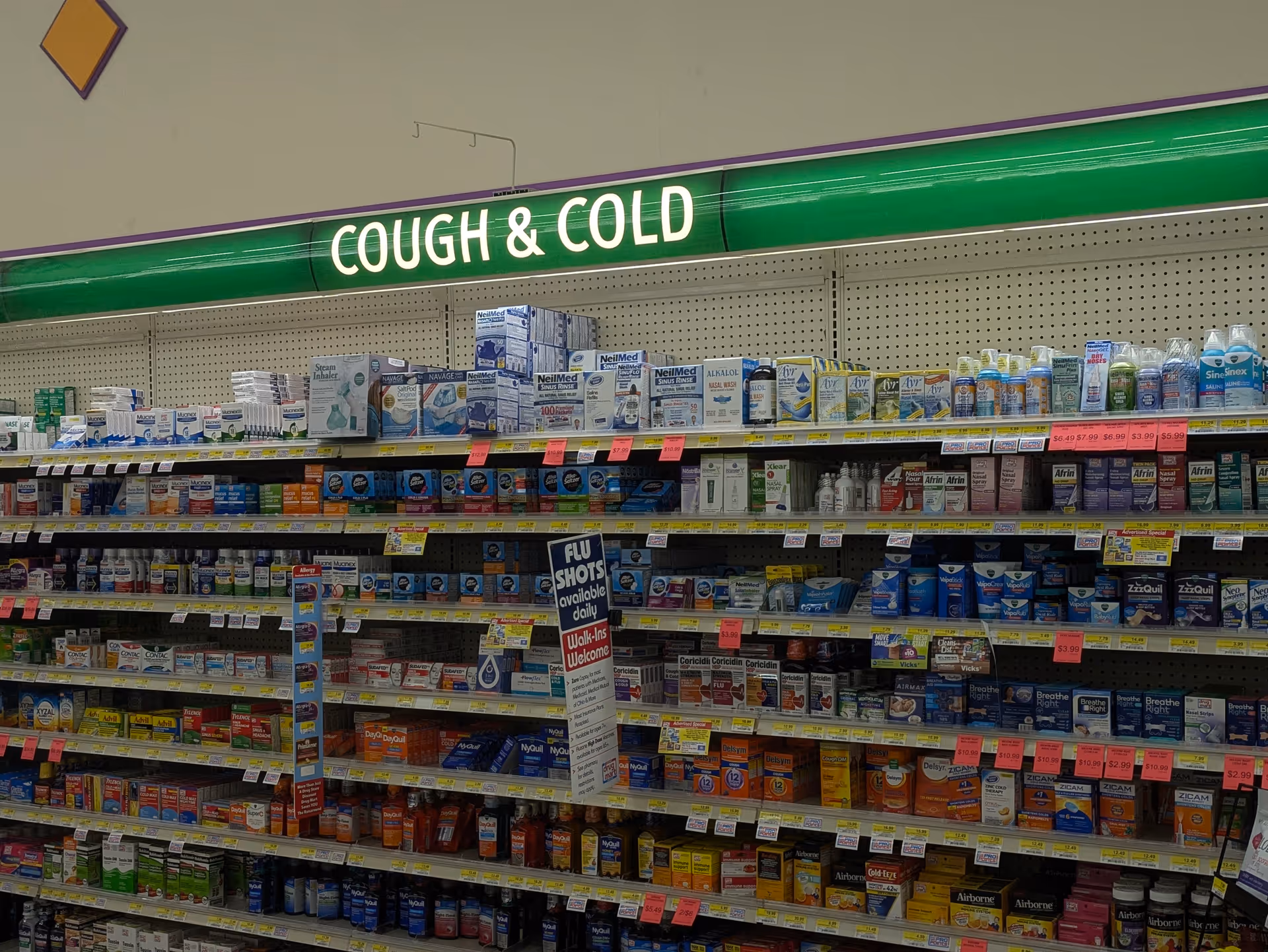 A pharmacy aisle filled with cough and cold medicines under a green sign.