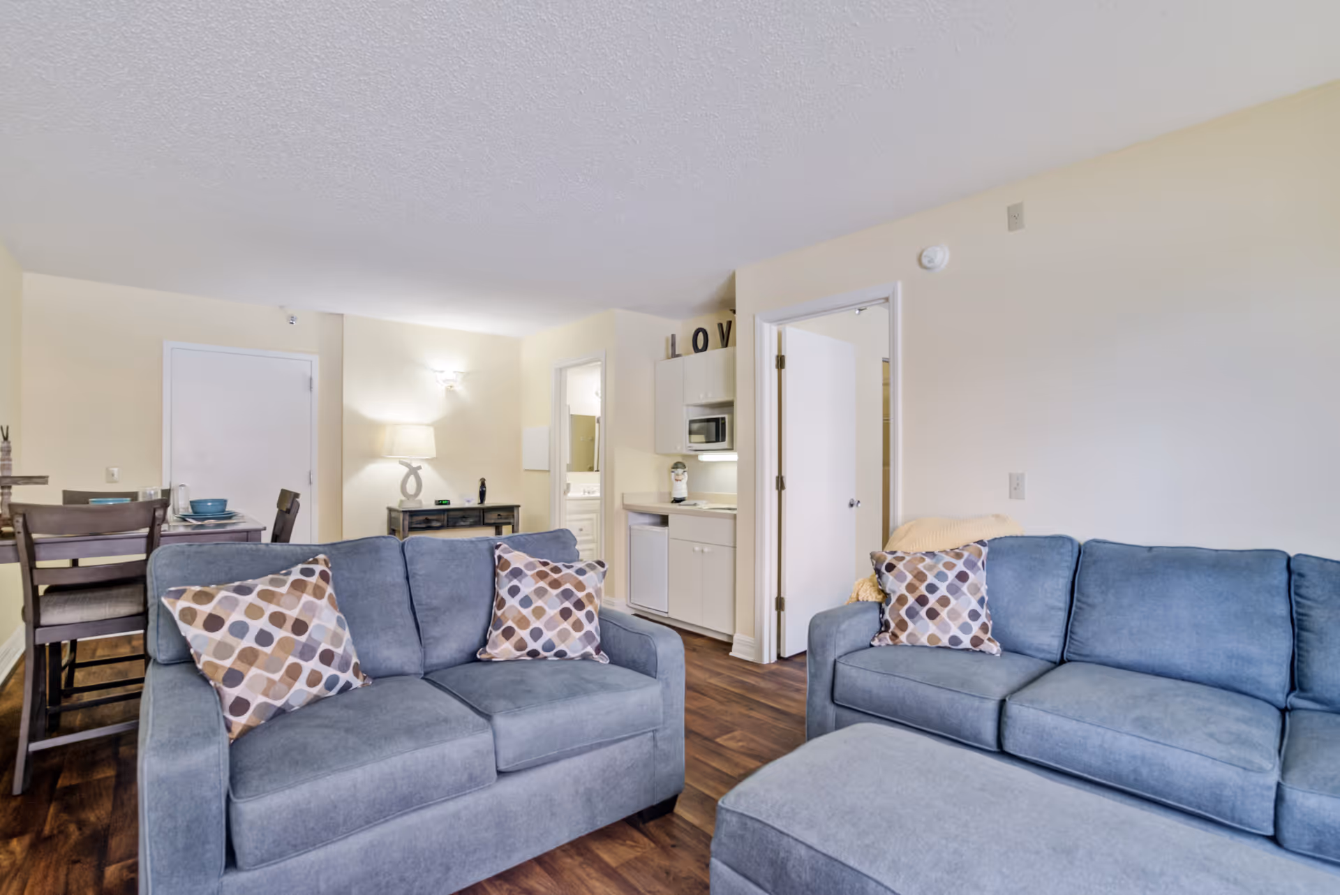Bright living area with blue sofas, a dining table, and a compact kitchen.