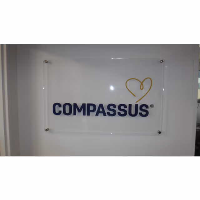 Wall-mounted acrylic sign reads COMPASSUS with a heart logo.