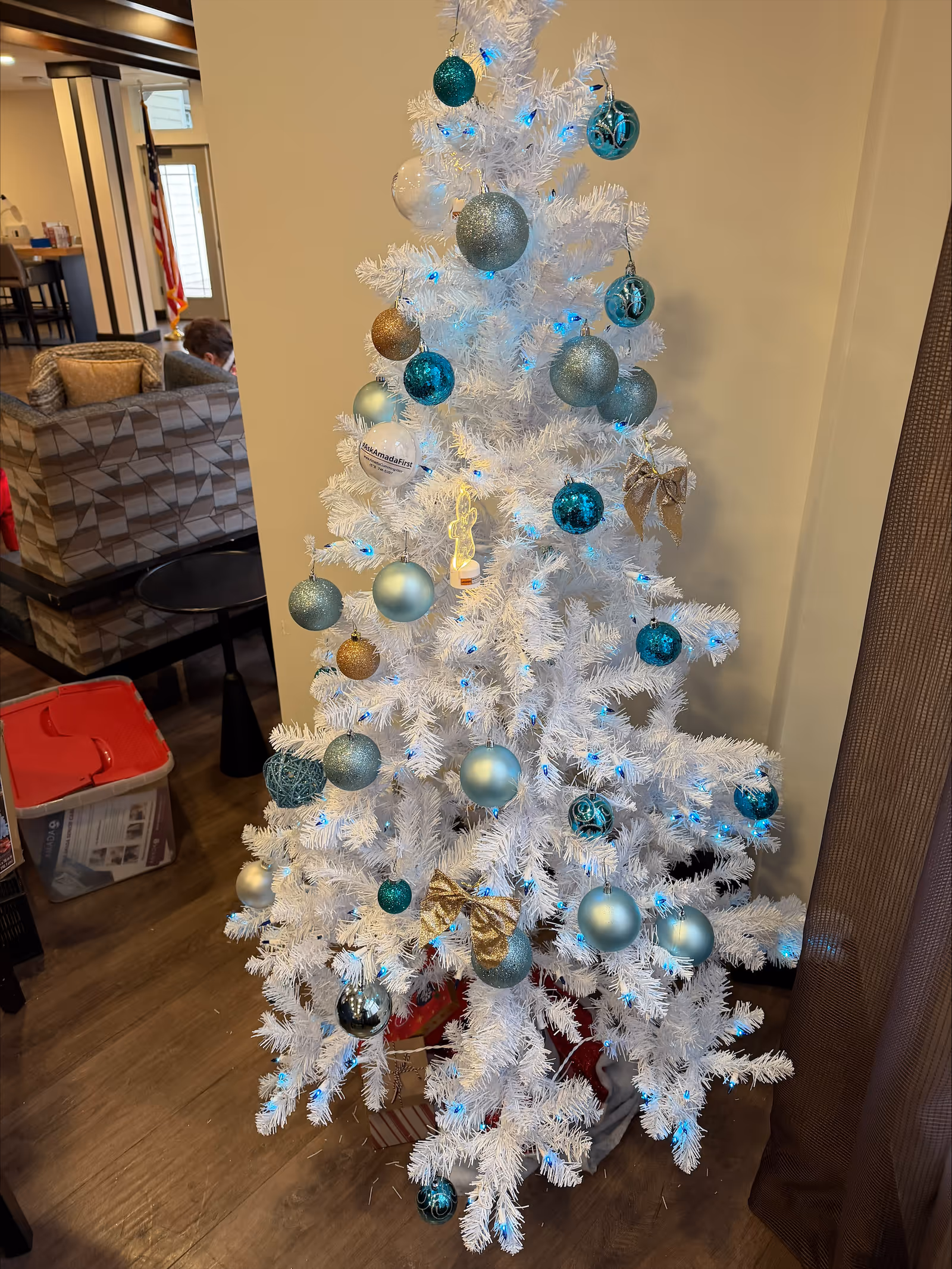White Christmas tree with blue and silver ornaments and lights in a senior living facility lounge.