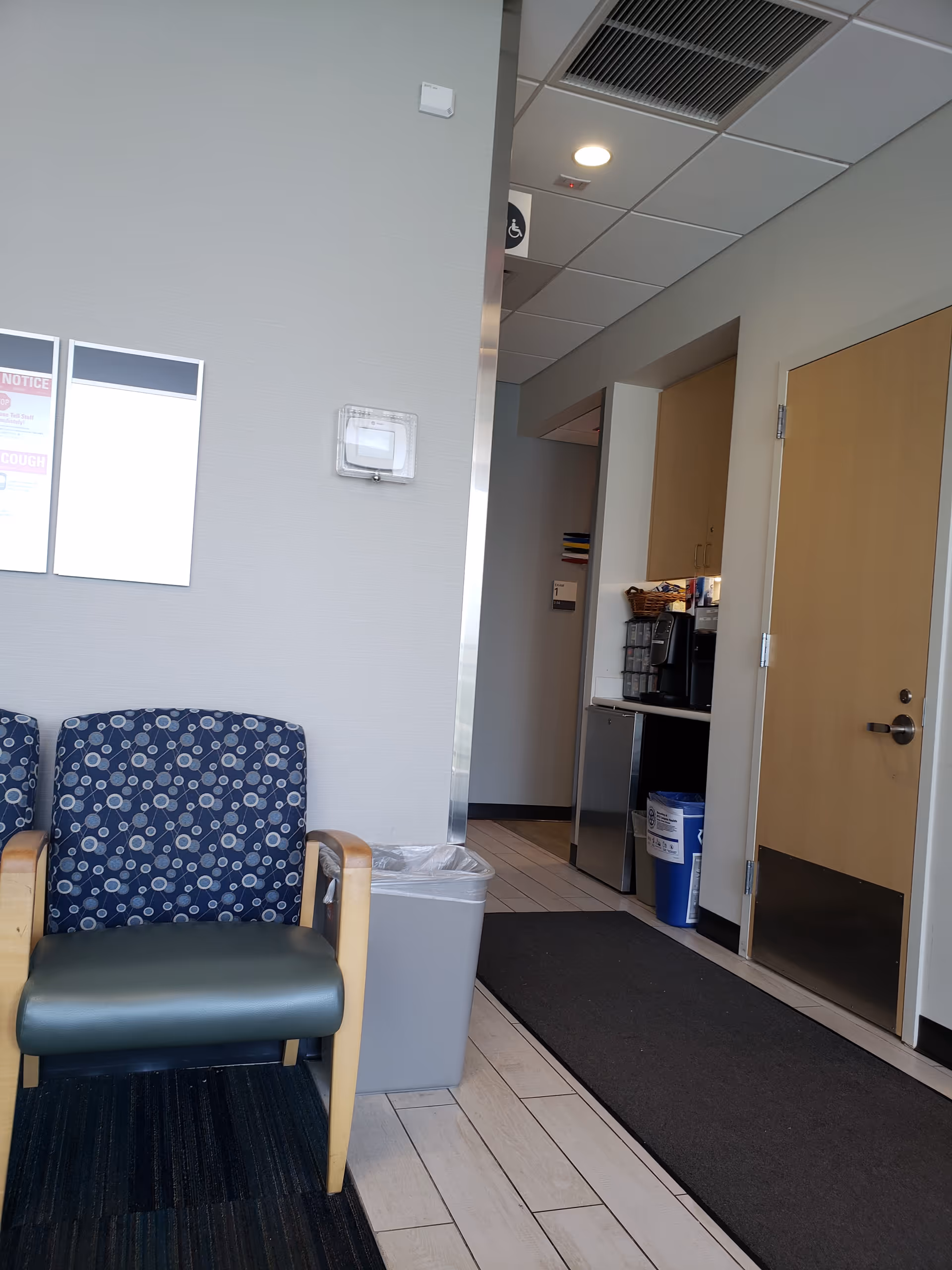 Interior waiting area with blue patterned chairs, a trash can, and a coffee station.