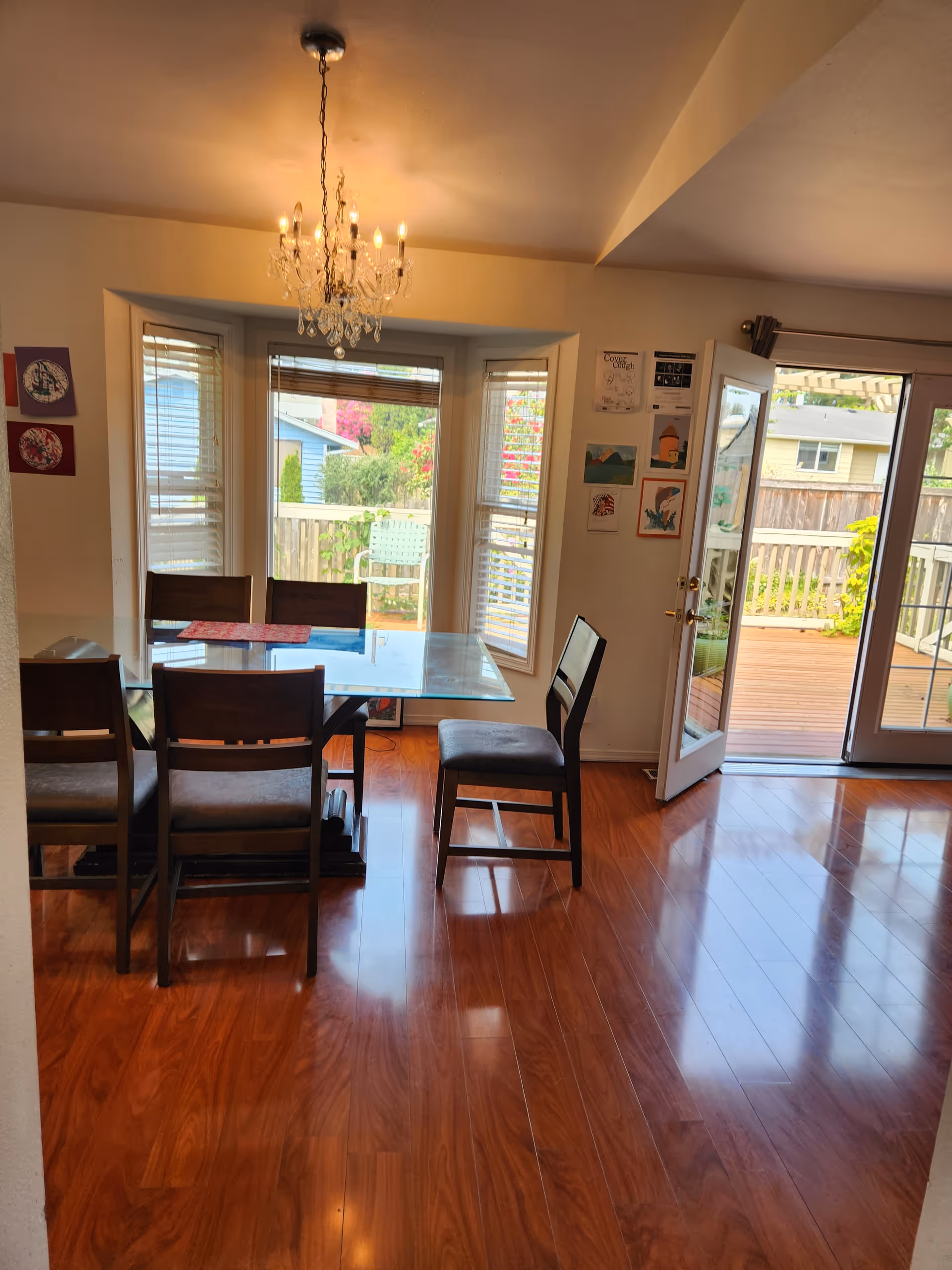 Bright dining room with glass table, chairs, chandelier, bay windows, and sliding door to deck