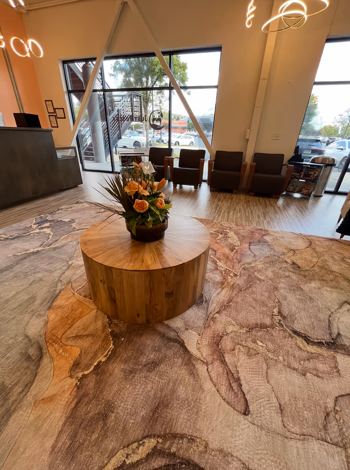 Modern lobby with a round wooden pedestal table and floral centerpiece.