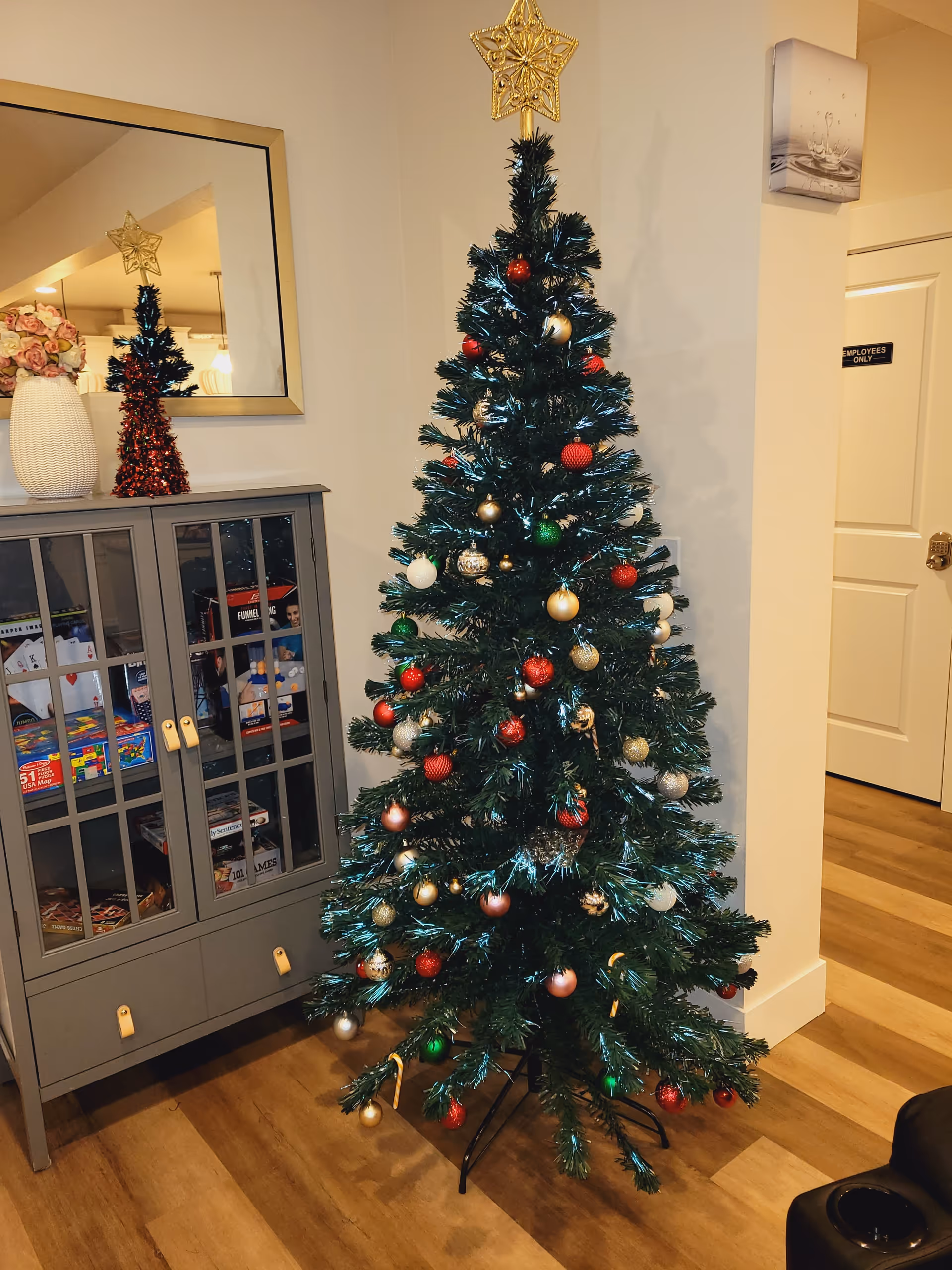 Indoor living area featuring a decorated Christmas tree beside a gray display cabinet and mirror.