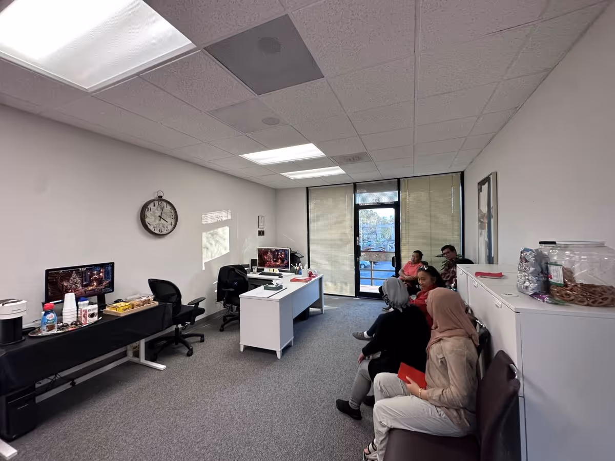 Interior office-like lobby with desks, computers, a wall clock, and residents seated.
