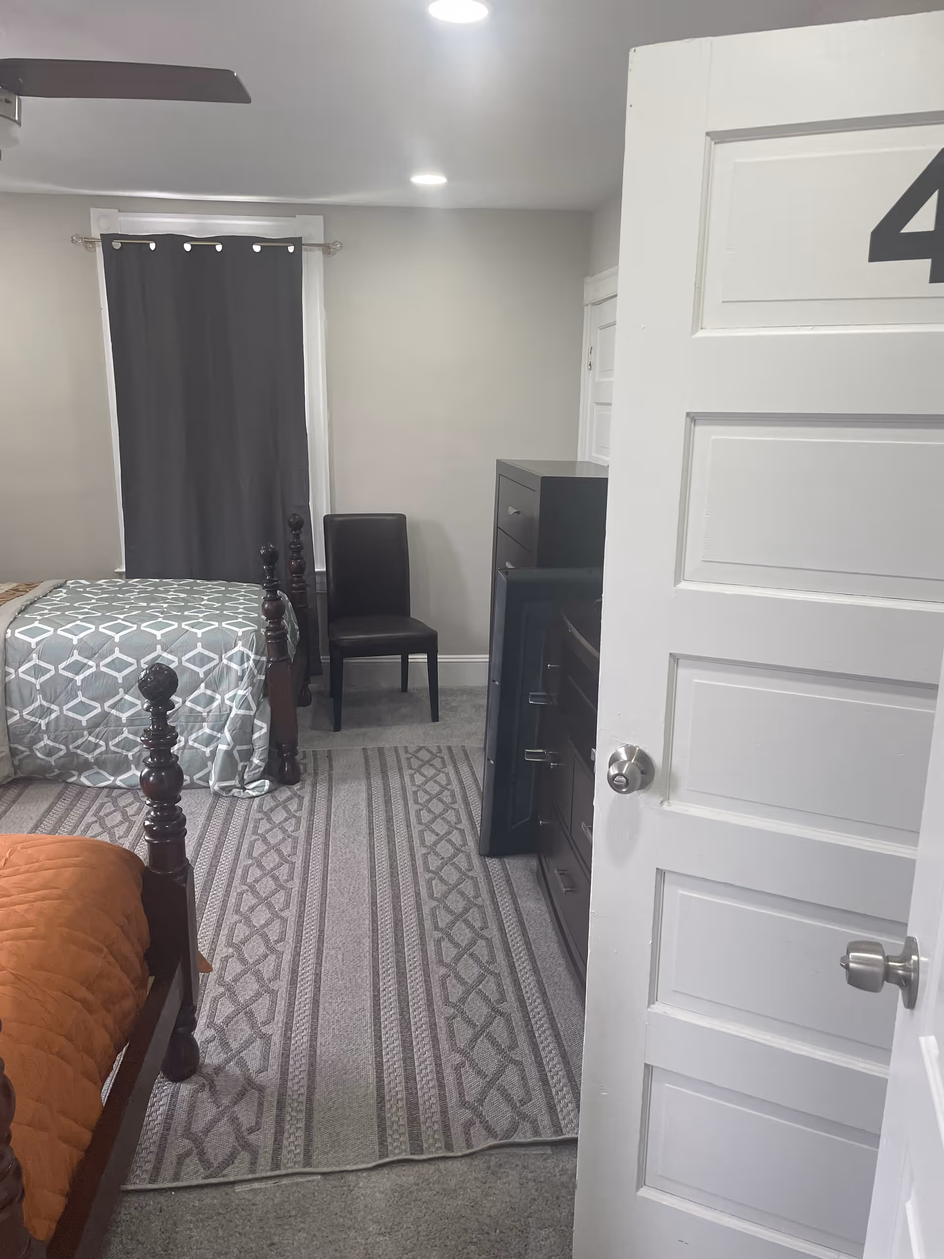 A senior living bedroom with a bed, dresser, chair, and dark curtain.