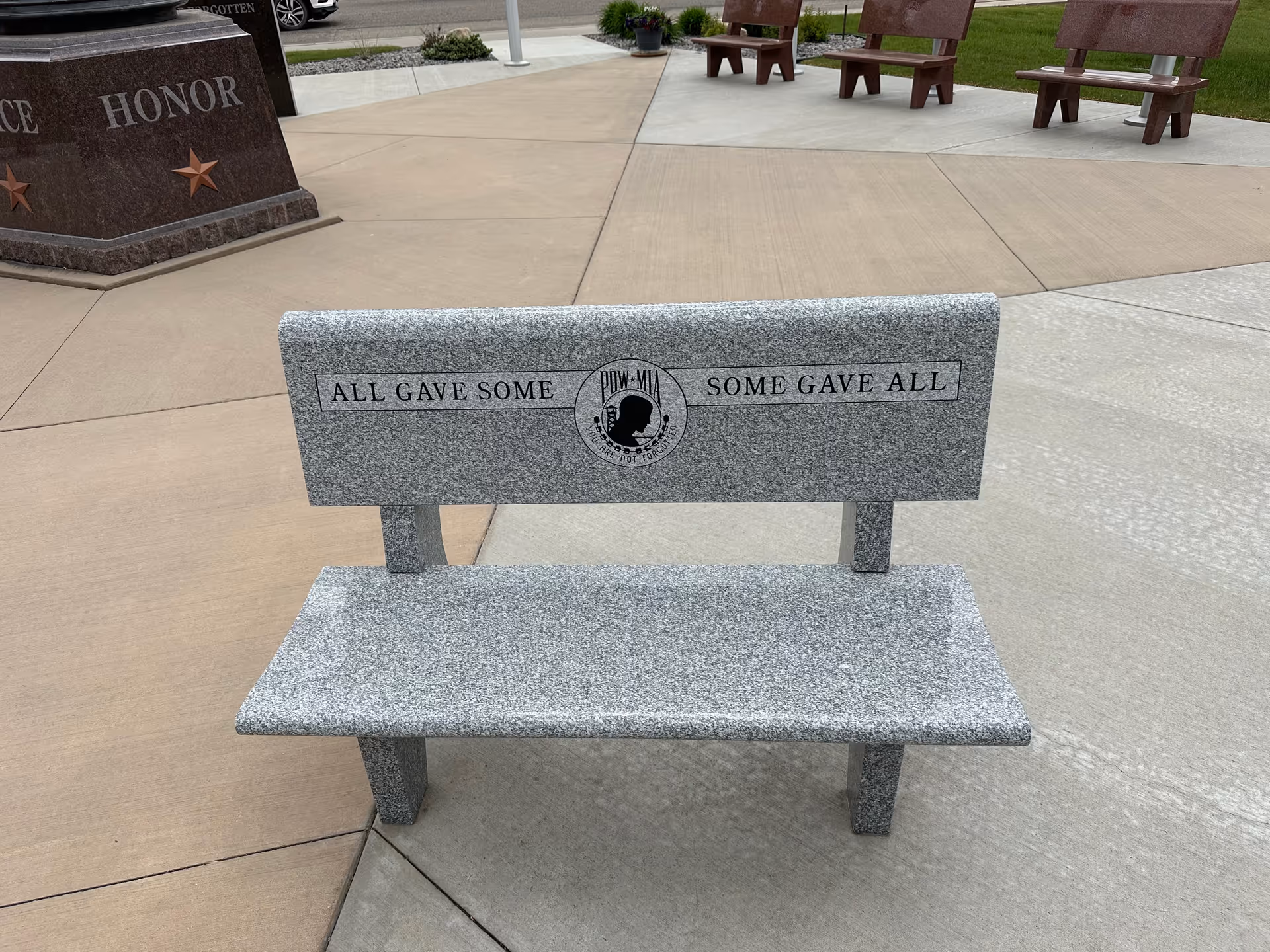 Granite bench engraved with All Gave Some; Some Gave All in an outdoor memorial plaza.