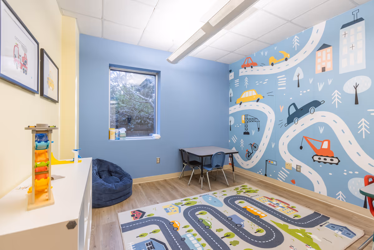 Colorful children's playroom with road-themed mural, rug, small table and chairs, and toy storage.