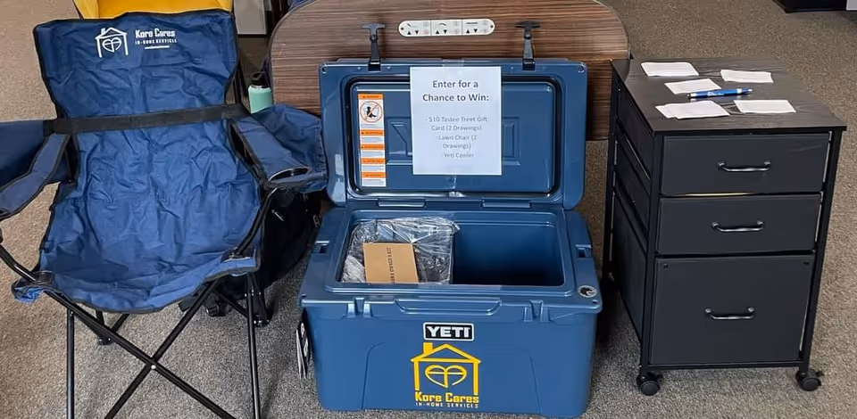 Blue Kore Cares cooler sits beside a folding chair and a black filing cabinet.