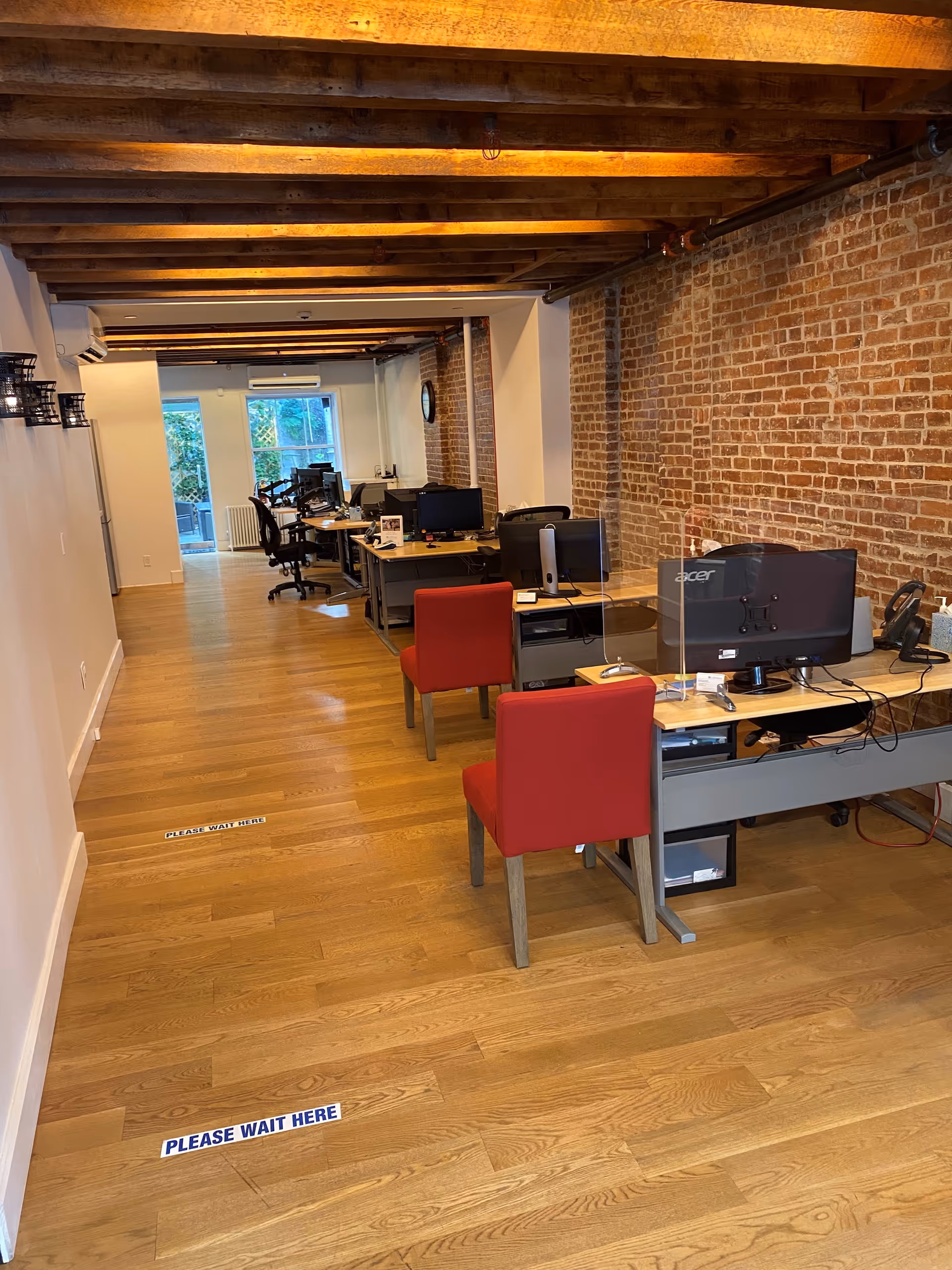 Interior office area with desks, computers, and red chairs along brick walls