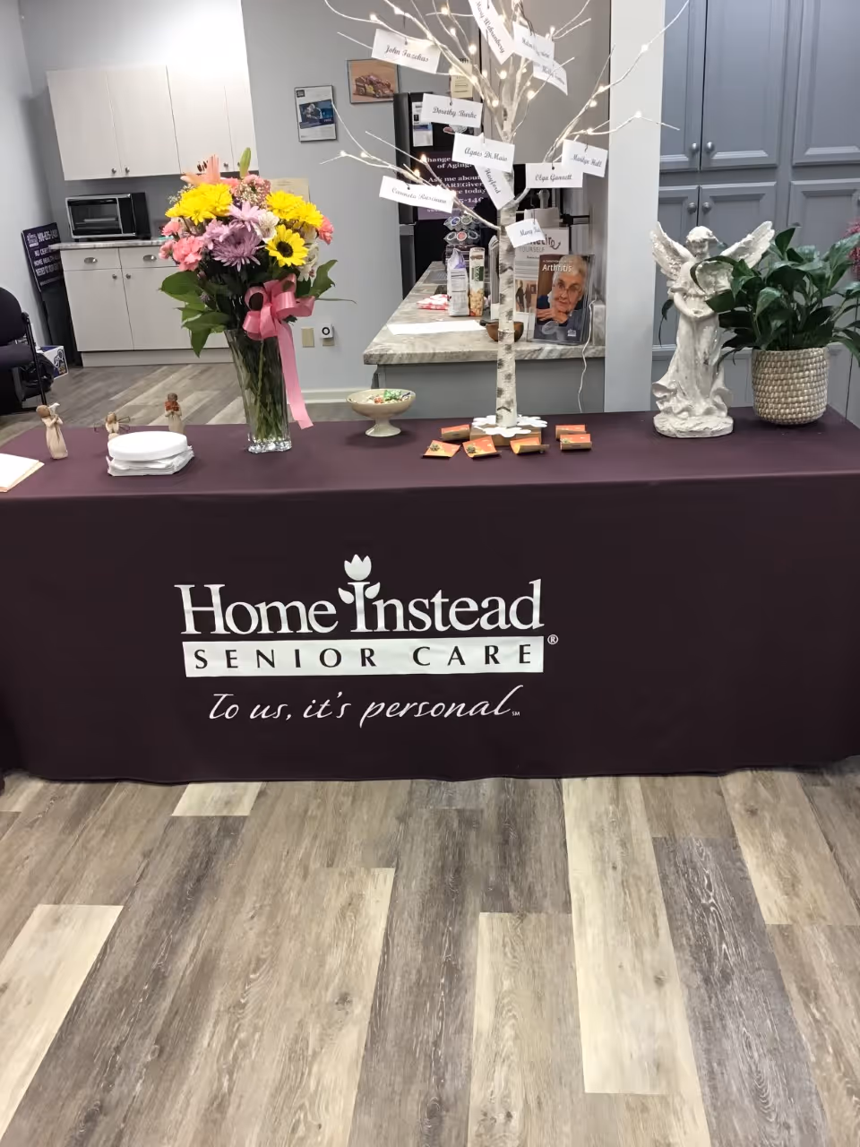 A table with Home Instead Senior Care branding sits inside a modern facility lobby.