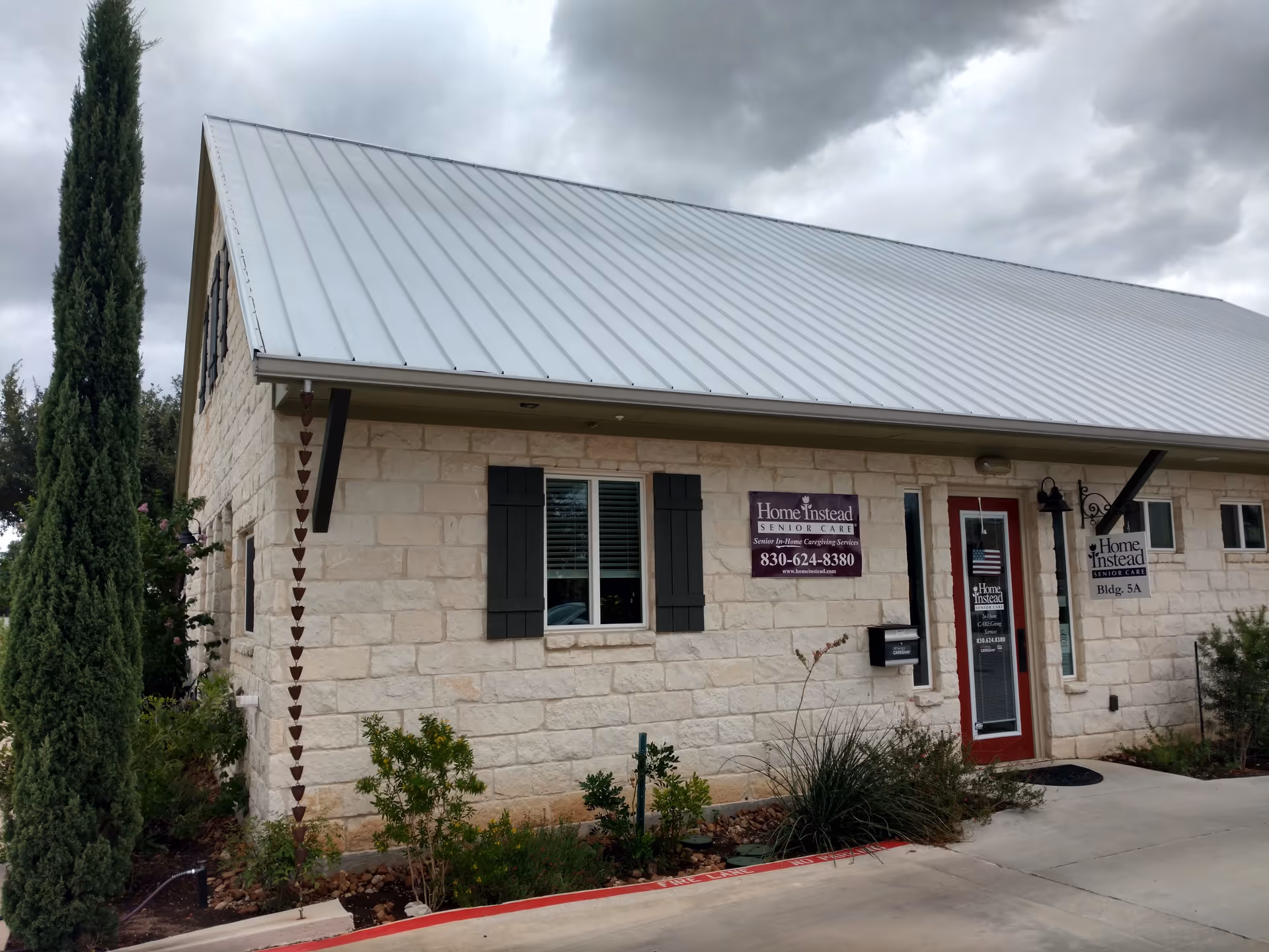 Stone exterior building with metal roof, red front door, and Home Instead signage.