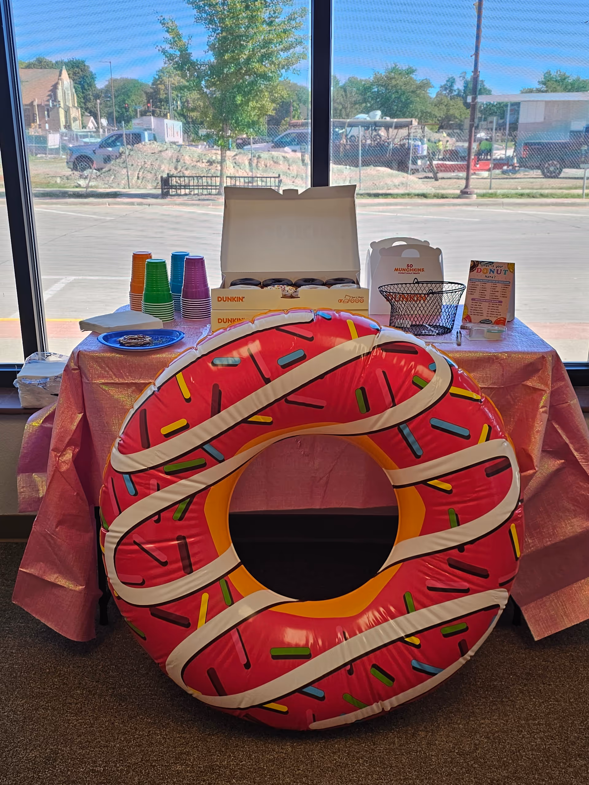 Interior scene with a festive table, donuts, cups, and a large inflatable donut float.