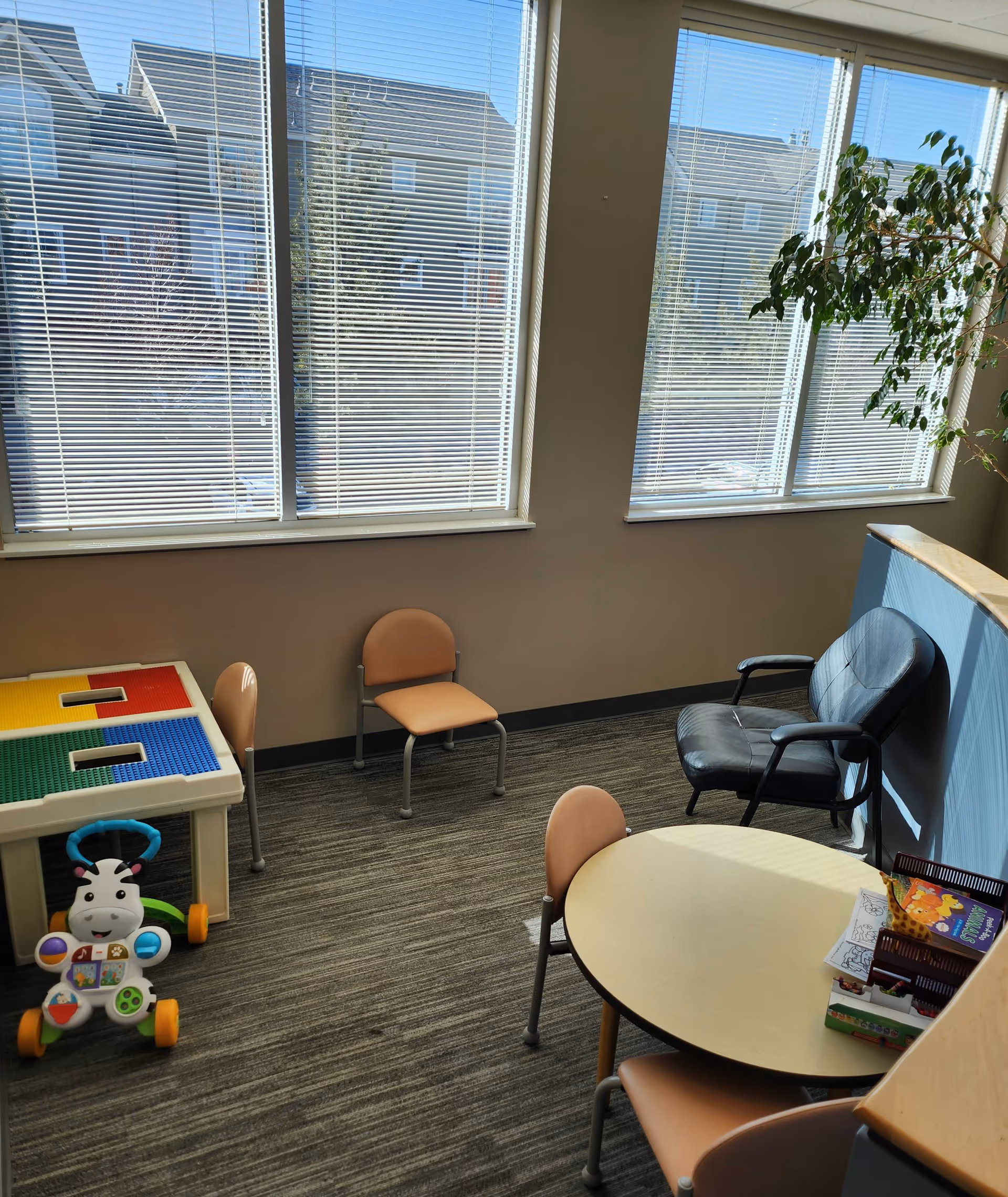 Bright indoor activity area with table, small chairs, a black office chair, and a plant.