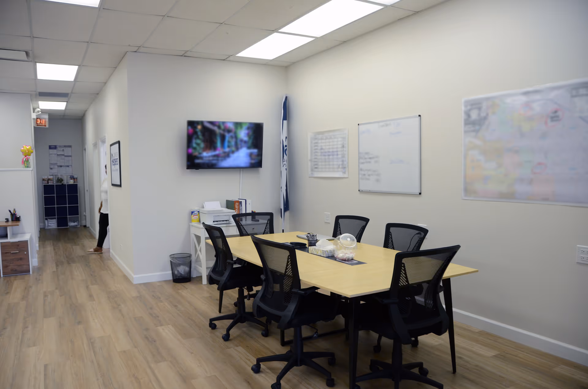 Modern conference room interior with a central table, chairs, whiteboards, and a wall-mounted TV.