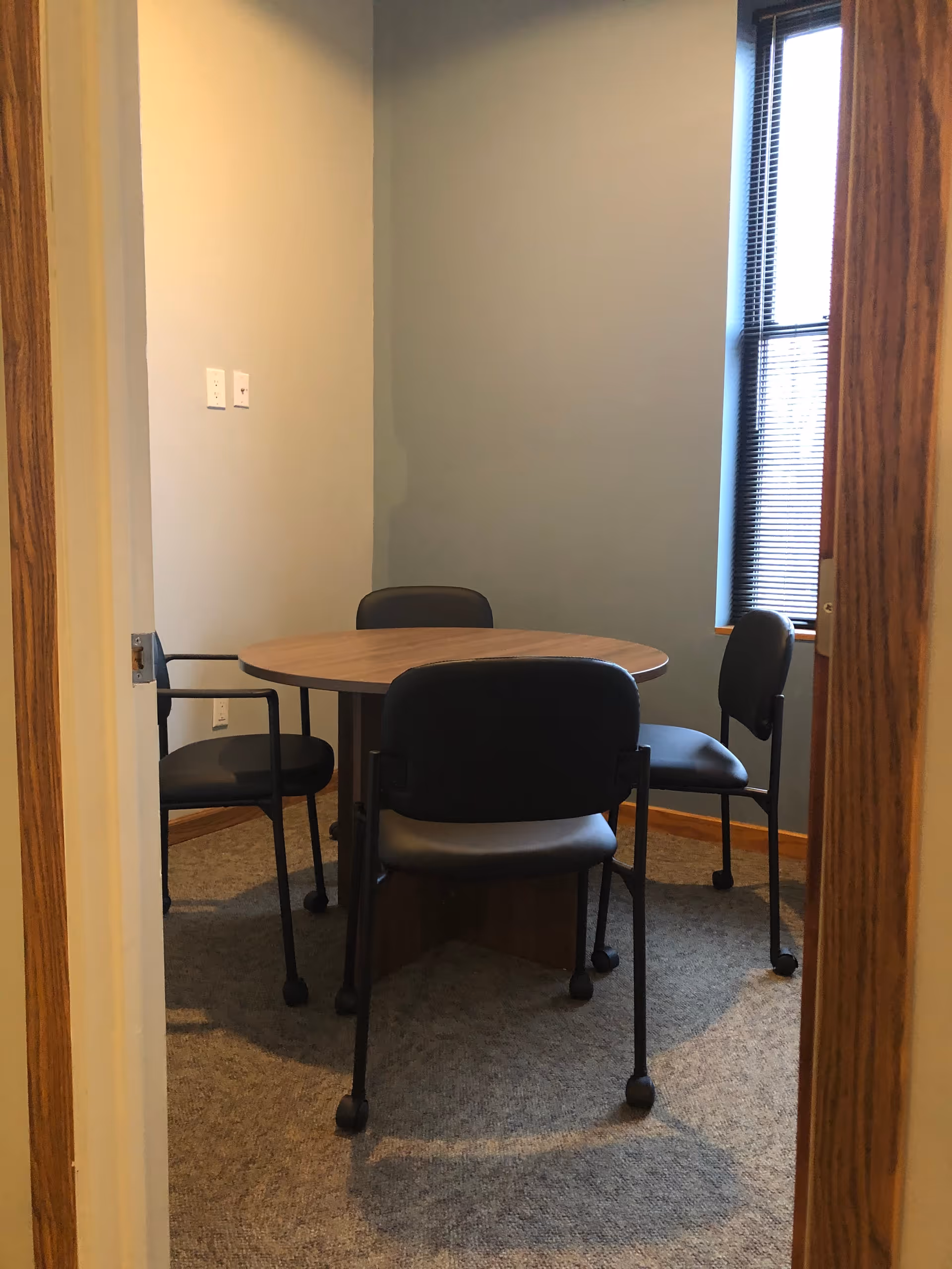 Small round table with four chairs in a carpeted dining room by a window.