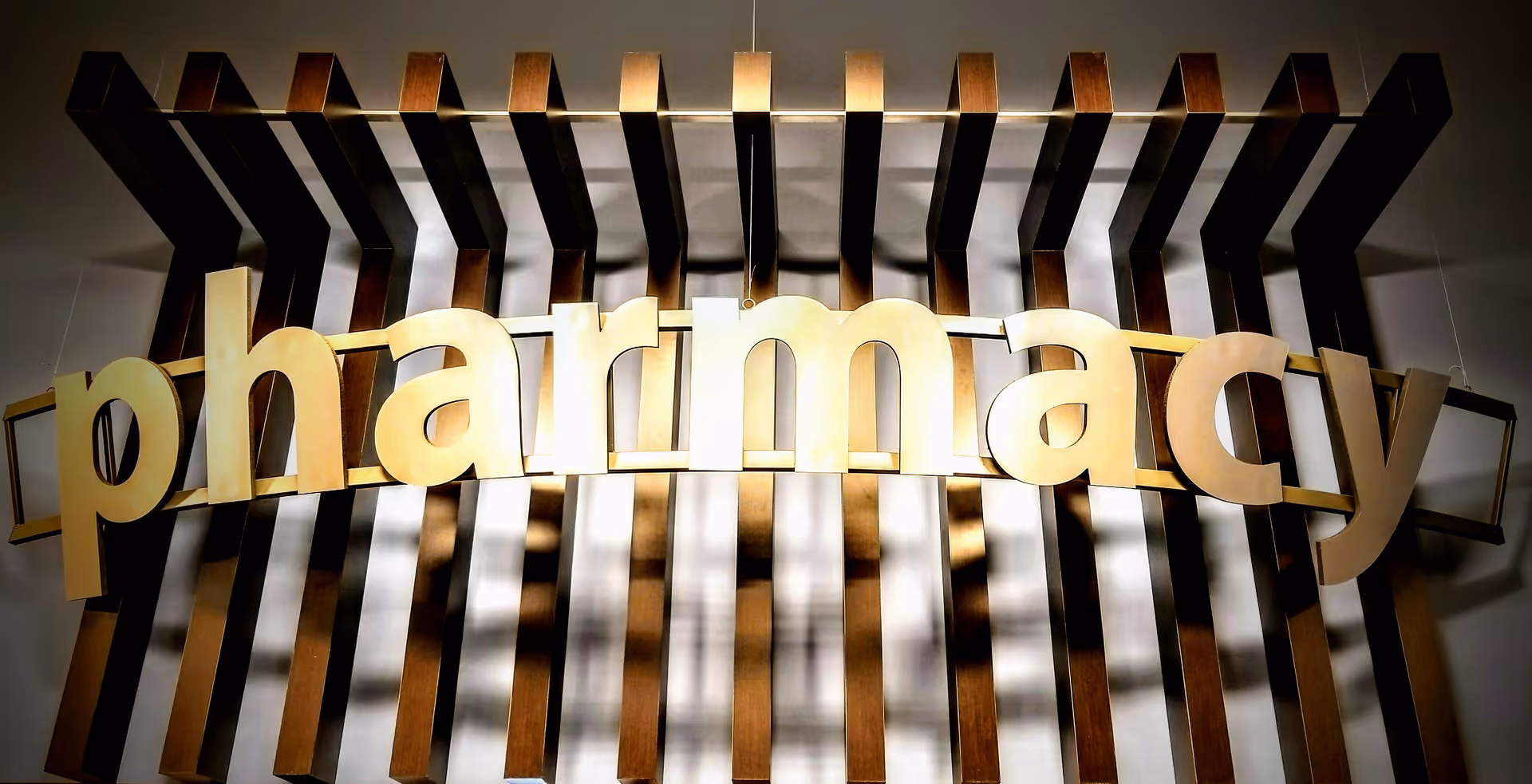 A gold 'pharmacy' sign spans a wall with decorative wooden slats indoors.
