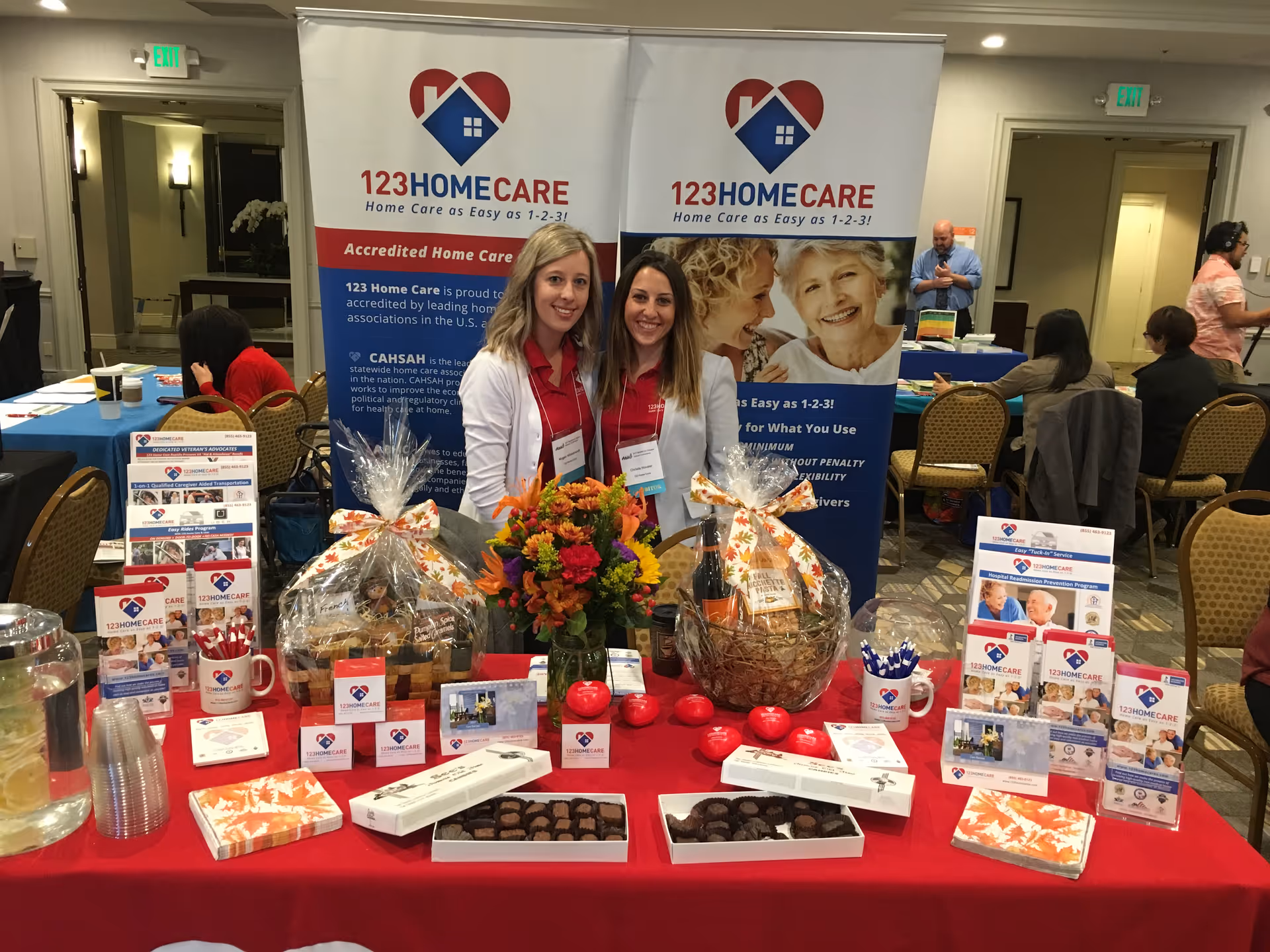 Two women pose behind a promotional table at a TheKey Home Care booth.